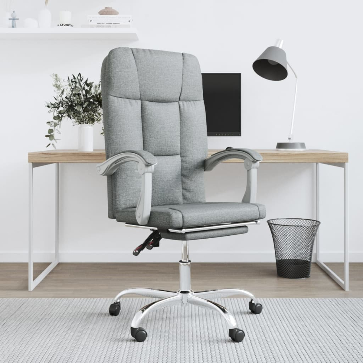 Ein grauer Bürostuhl steht vor einem Schreibtisch mit Computer und Lampe. Eine Pflanze und ein Mülleimer sind ebenfalls vorhanden.