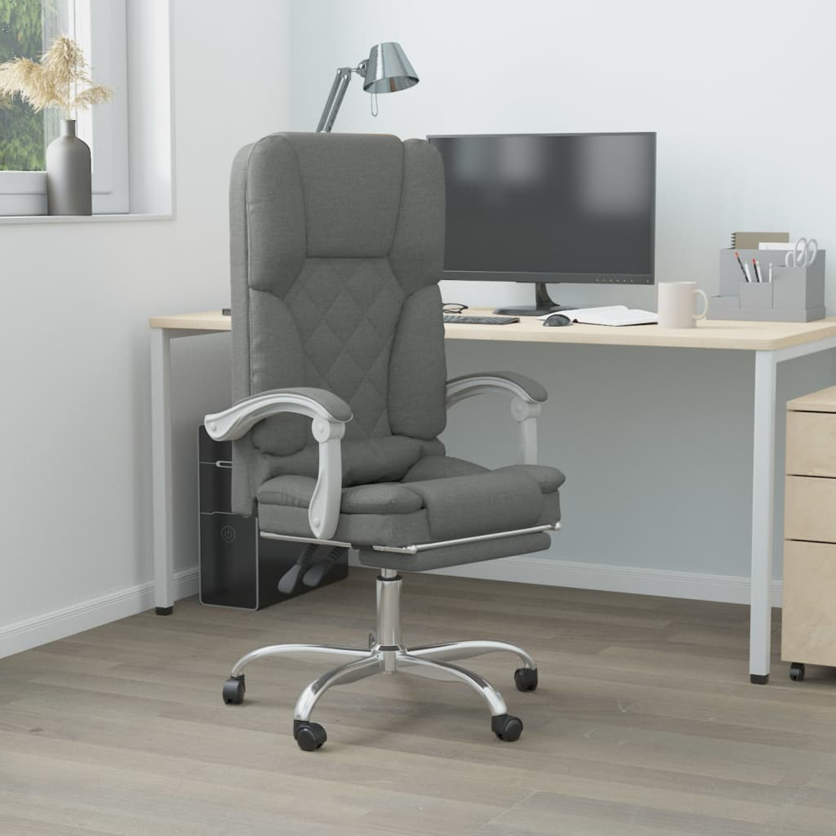 Ein grauer Bürostuhl mit silbernen Beinen und ein Computertisch mit Monitor, Lampe und Zubehör.
