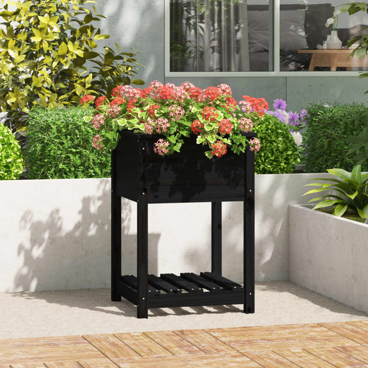 Eine schwarze Holzpflanzkiste mit roten und rosa Blumen. Sie steht auf einer Terrasse mit Grün im Hintergrund.