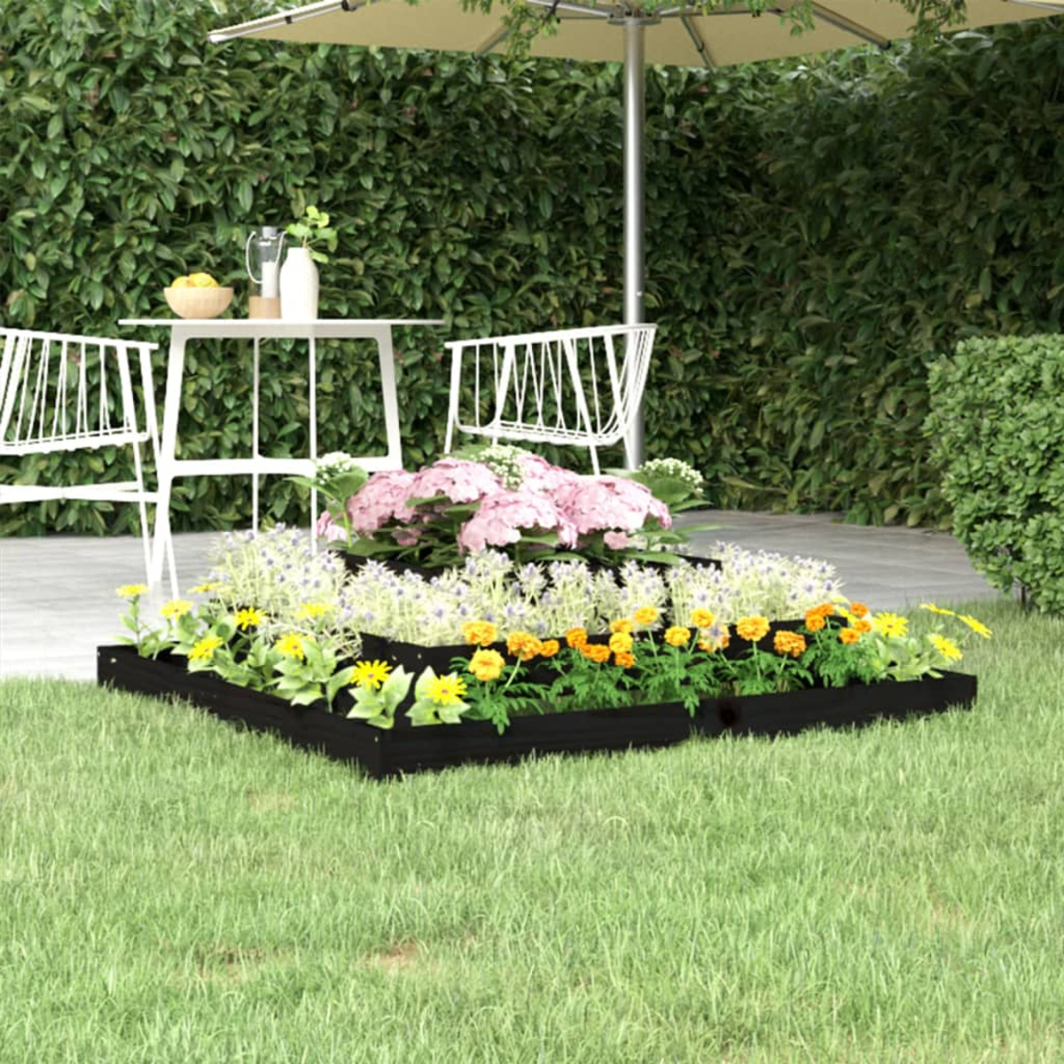 Gartenszene mit weißen Stühlen, Tisch und Blumen in Hochbeeten. Eine grüne Hecke im Hintergrund und ein Sonnenschirm.