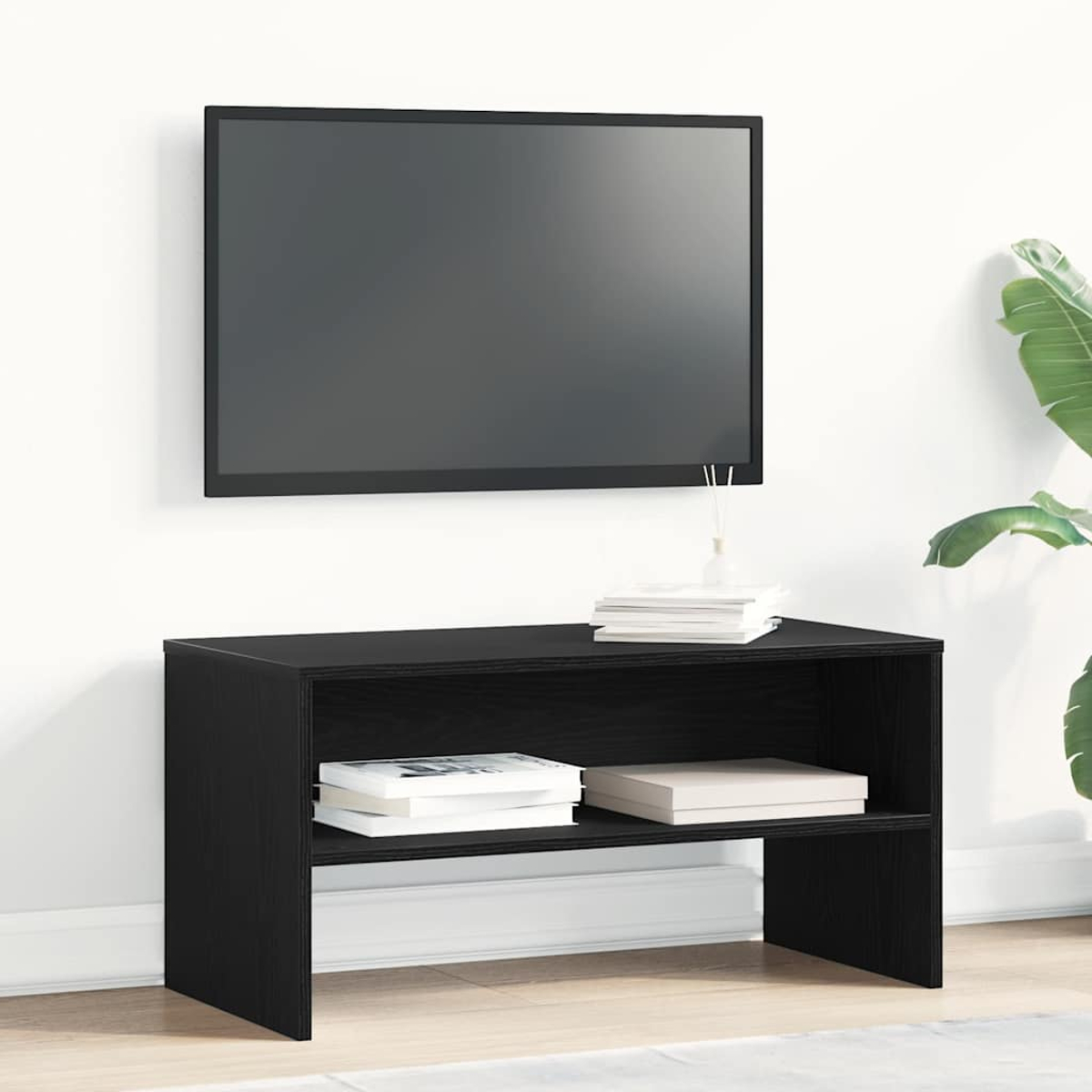 Un mueble de TV negro con un televisor en la pared. Libros y un jarrón encima. Una planta a la derecha.