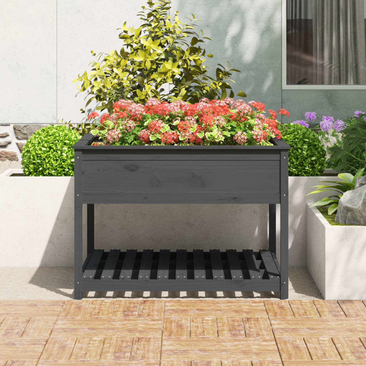 Dunkelgraue Holzkasten mit roten und rosa Blumen, auf einer gefliesten Terrasse. Hintergrund mit Pflanzen und einer Wand.