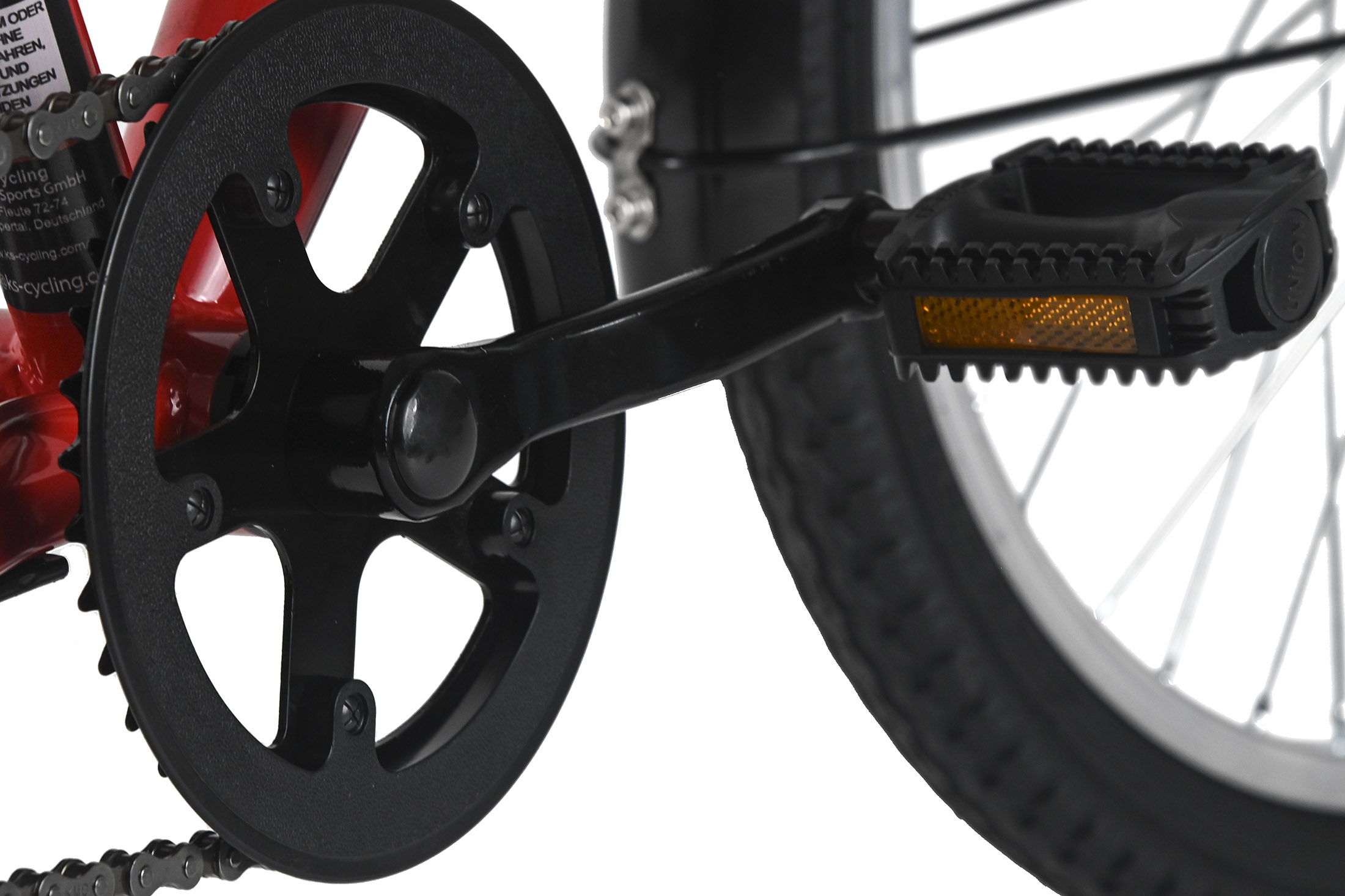 Nahaufnahme von Fahrradkurbel und -pedal. Schwarzes Kettenblatt, Pedal mit orangefarbenem Reflektor. Roter Rahmen sichtbar.