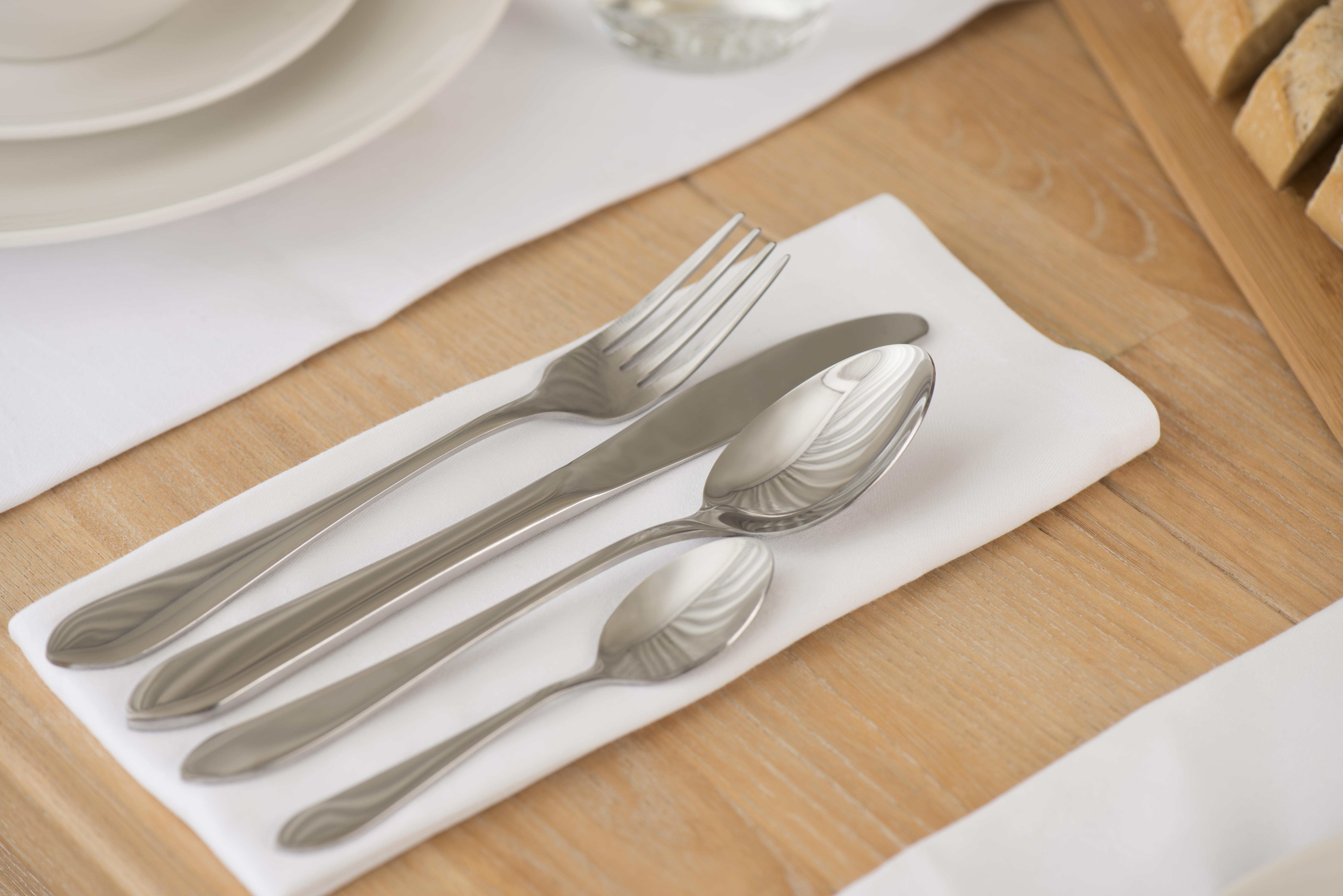 Table setting with silverware on a white napkin. Plates and bread slices are also visible. Wooden table.