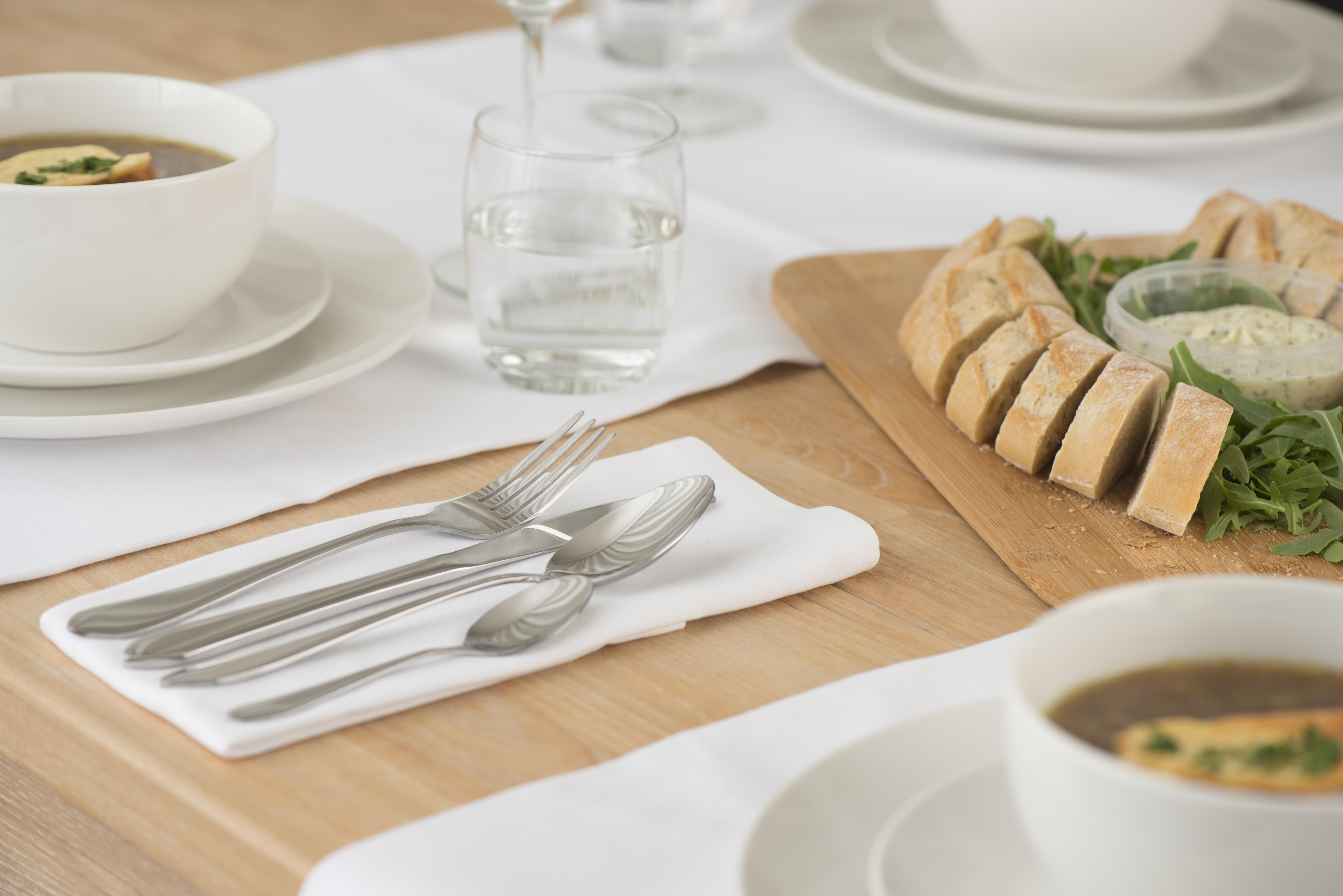 Table setting with soup, bread, and cutlery. Includes soup bowls, bread slices, and a glass of water.