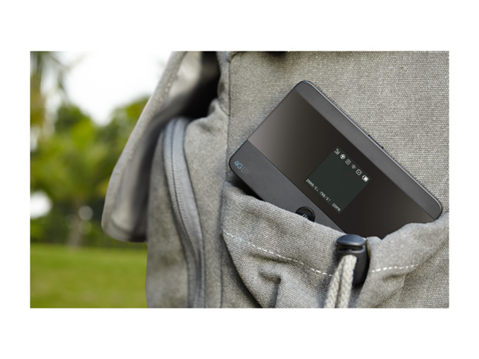 Ein schwarzer 4G-LTE-Mobil-Hotspot befindet sich in einer grauen Rucksacktasche. Der Hintergrund ist verschwommenes grünes Laub.