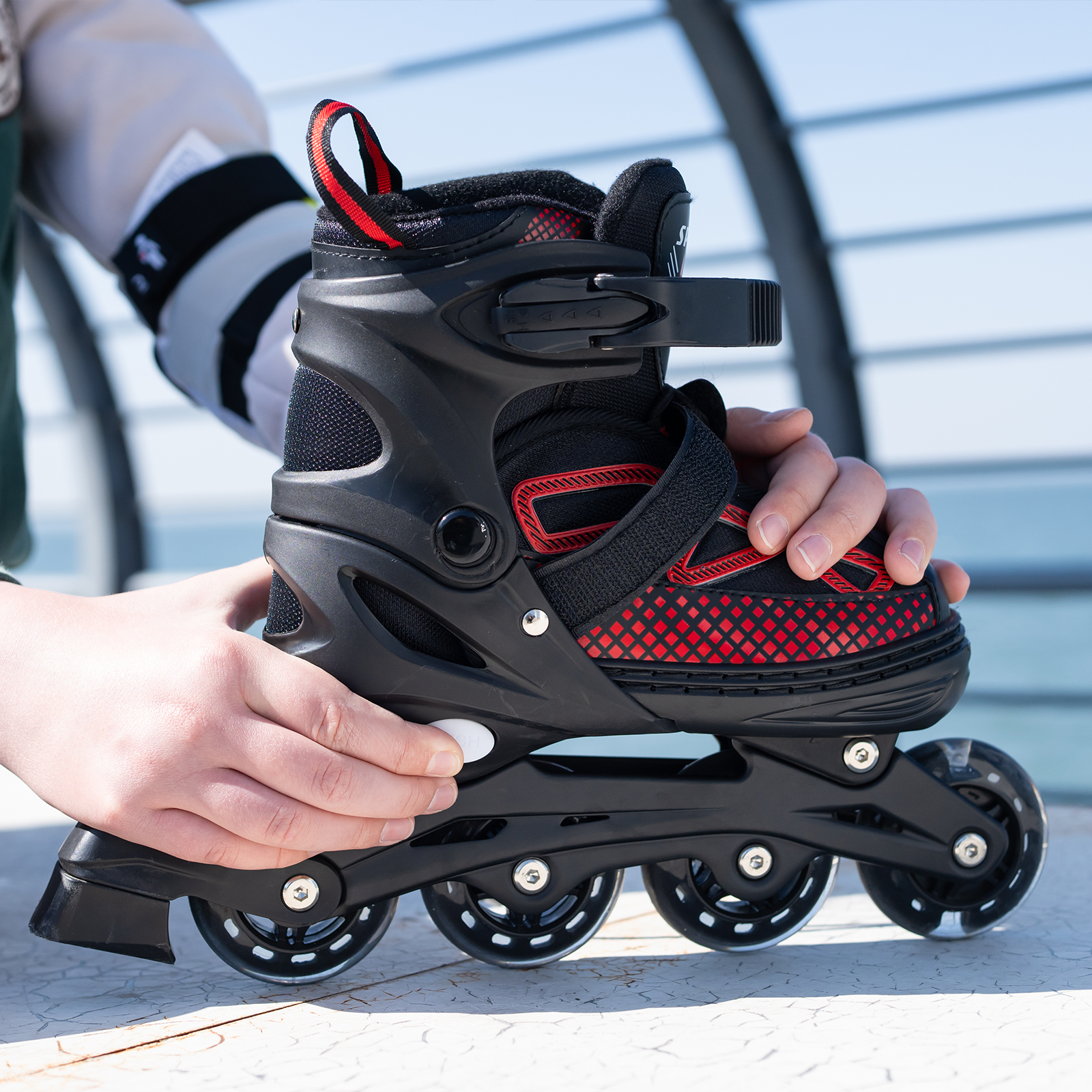 Patinete en línea negro y rojo sostenido por manos, sobre una superficie texturizada con fondo borroso.