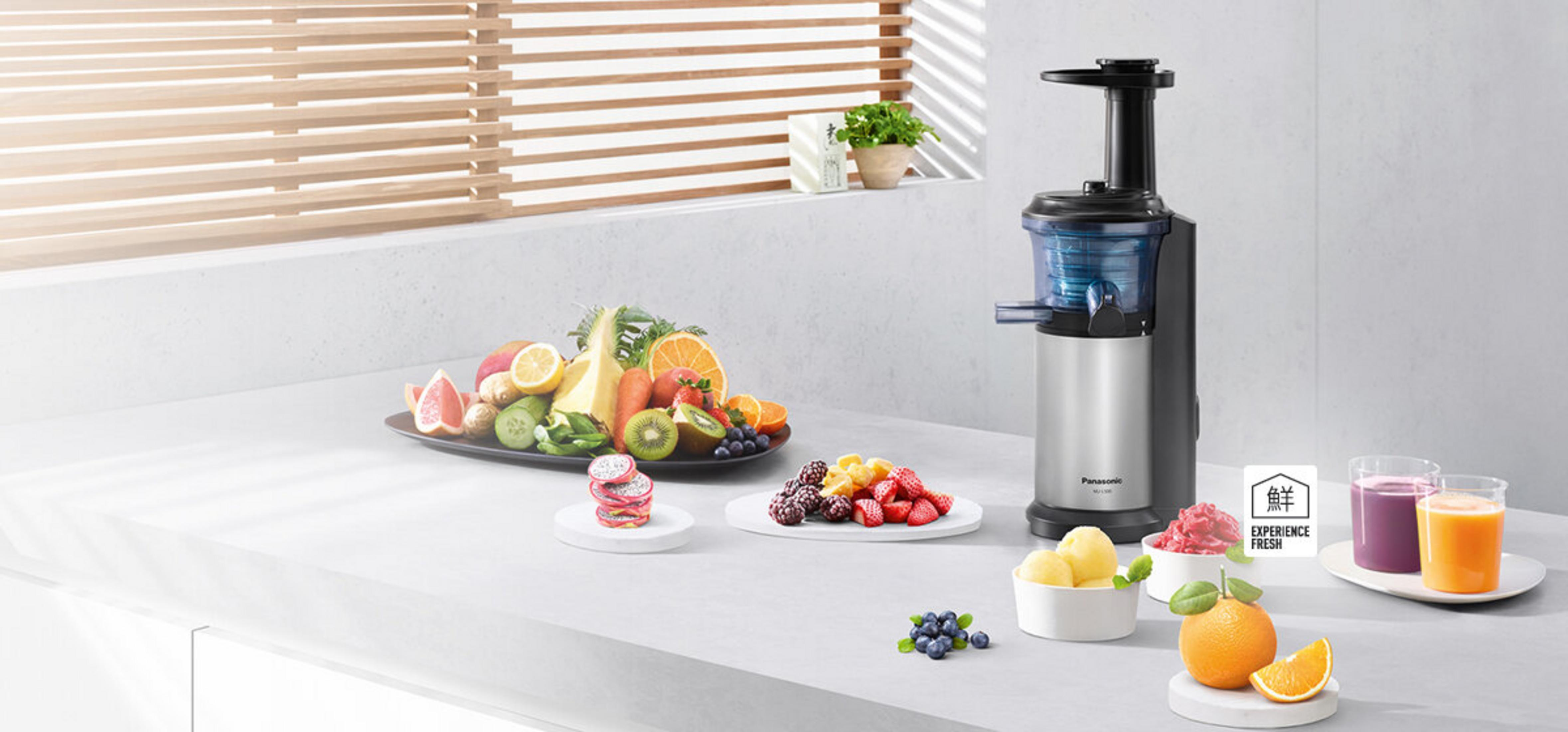 Wyrażarka do soku obok talerza z owocami i małymi miseczkami z owocami. Dwie szklanki soku i plasterek pomarańczy z przodu.