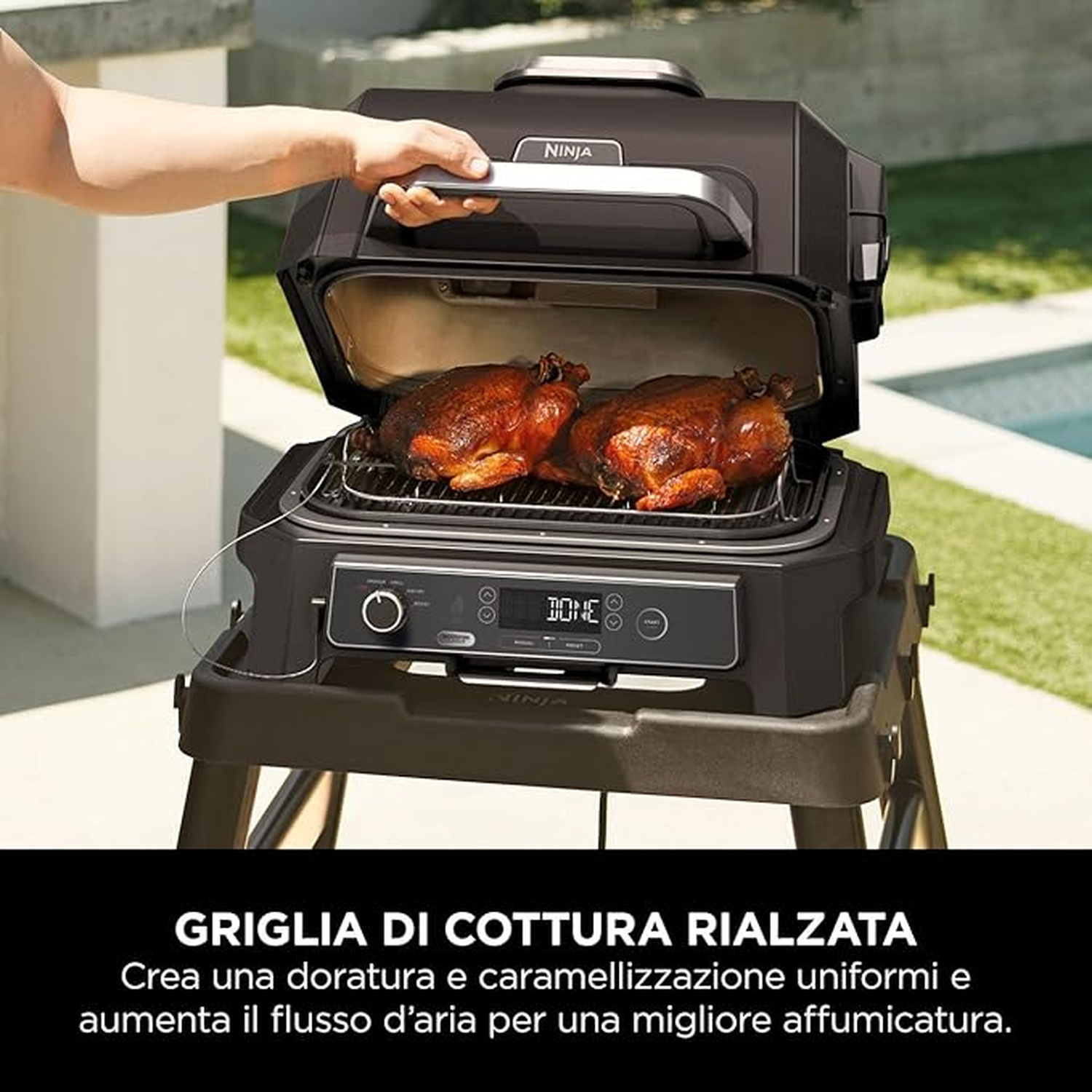 Ninja-Grill mit zwei gebratenen Hühnern. Eine Hand öffnet den Deckel. Der Grill steht draußen auf einem Ständer.