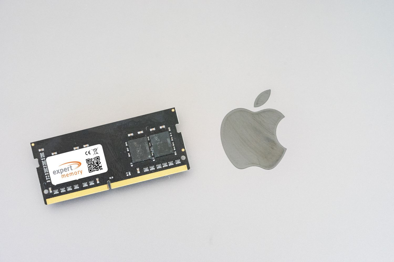 Schwarzes RAM-Modul neben einem grauen Apple-Logo auf weißem Untergrund. Das RAM ist mit 'expert memory' beschriftet.