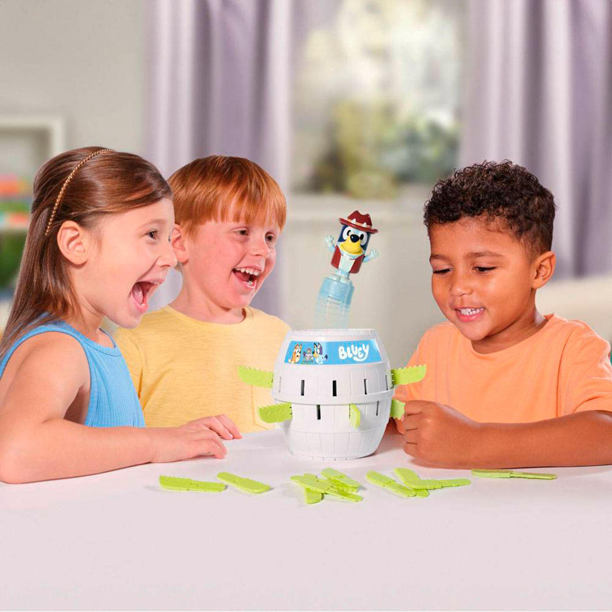 Tres niños juegan a un juego de Bluey, el juguete tiene forma de barril y un personaje de Bluey salta. Los niños están emocionados.