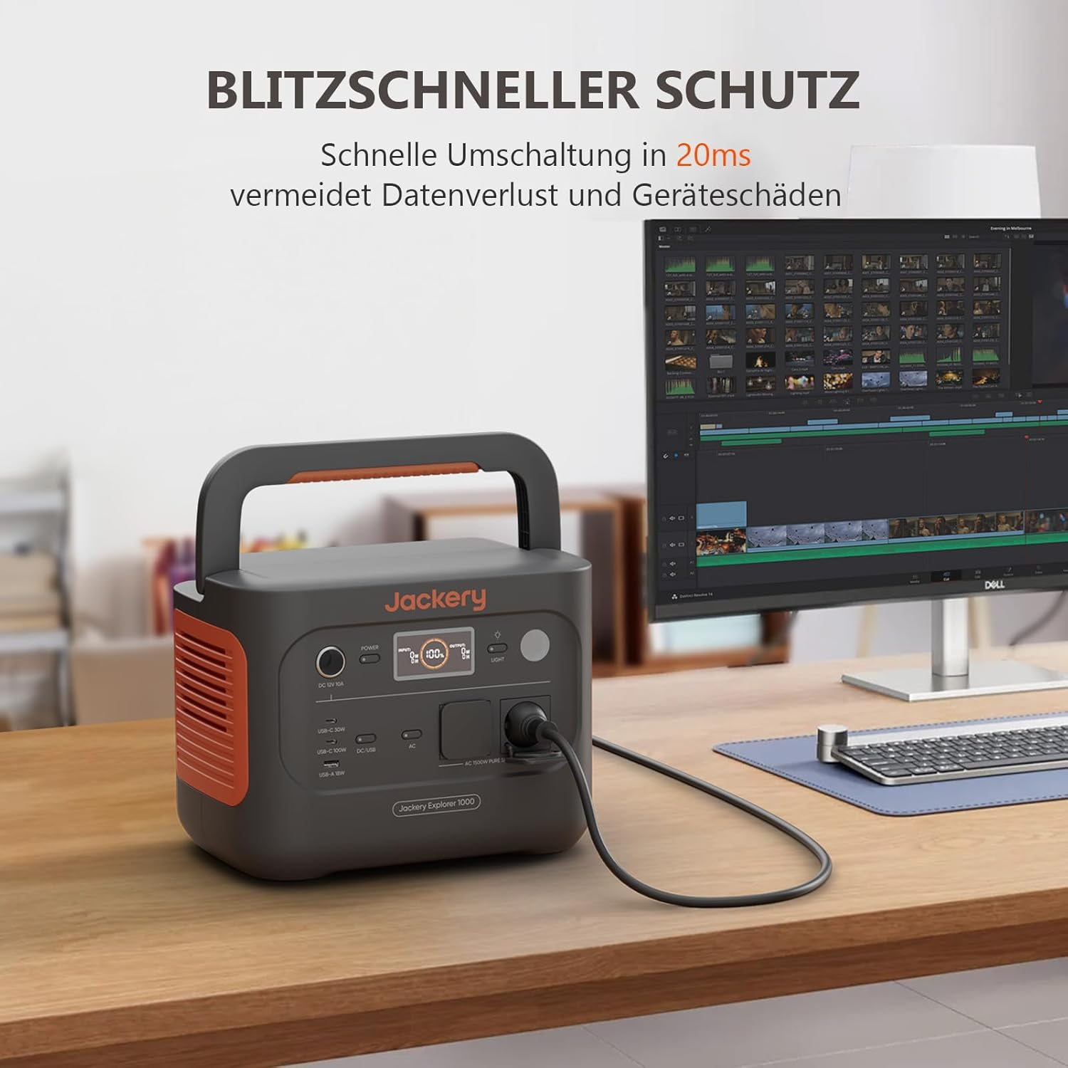 Eine Jackery Explorer 1000 Powerstation steht auf einem Schreibtisch. Ein Monitor zeigt Videobearbeitungssoftware.