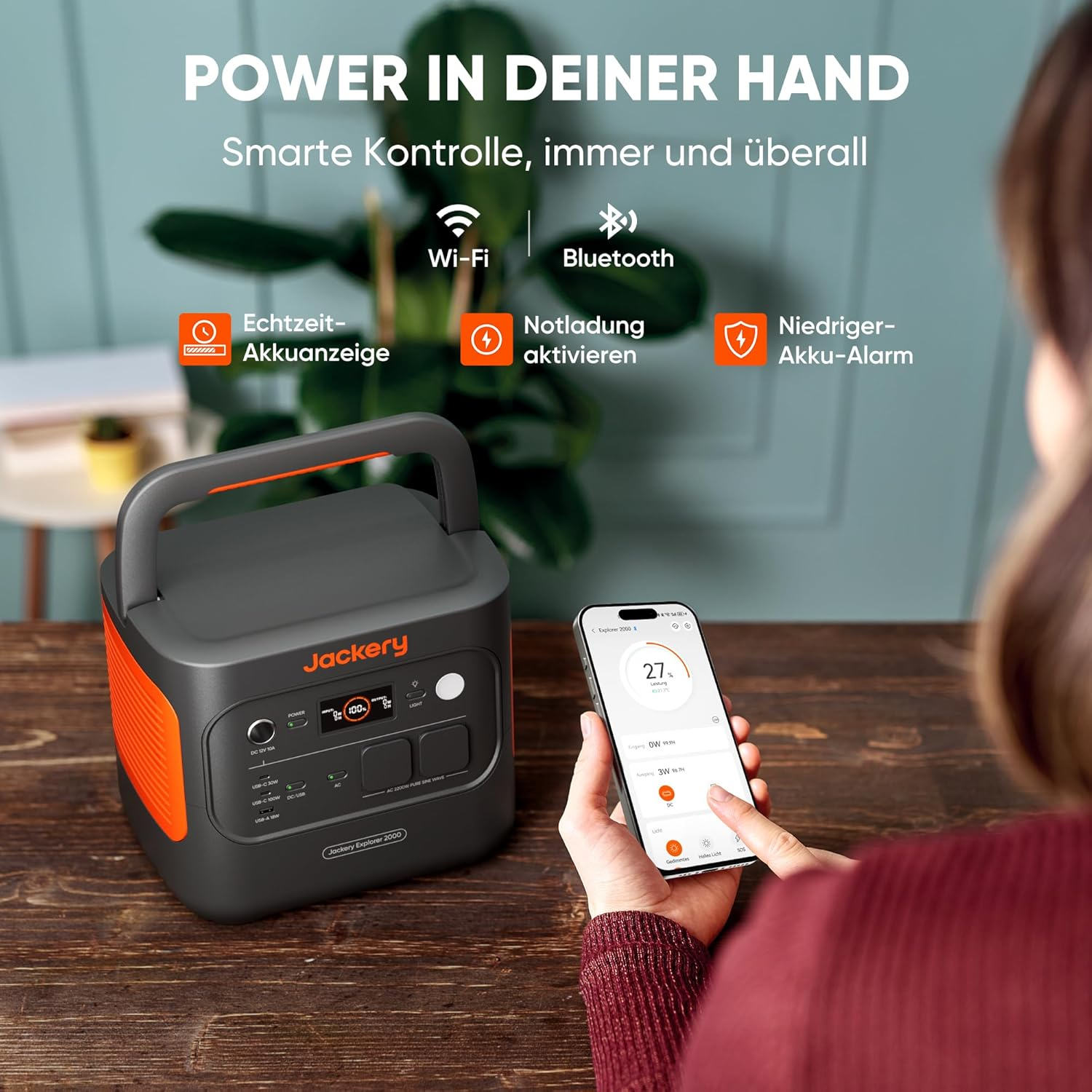Eine Person, die ein Telefon hält, das den Leistungspegel eines Jackery Explorer 2000 anzeigt. Die Powerstation ist schwarz und orange.