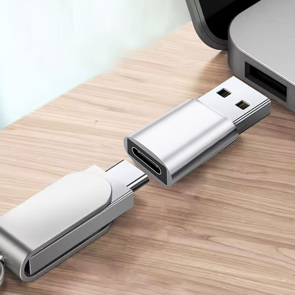 Srebrny adapter i złącze USB-C znajdują się w pobliżu laptopa. Adapter jest podłączony do portu USB-A.
