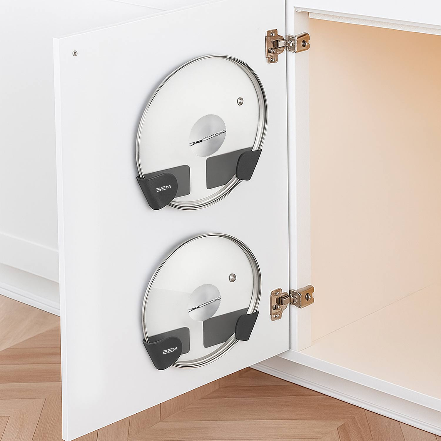 Weiße Schranktür mit zwei Topfdeckelhaltern. Jeder hält einen Glasdeckel. Der Schrank ist geöffnet und gibt das Innere frei.