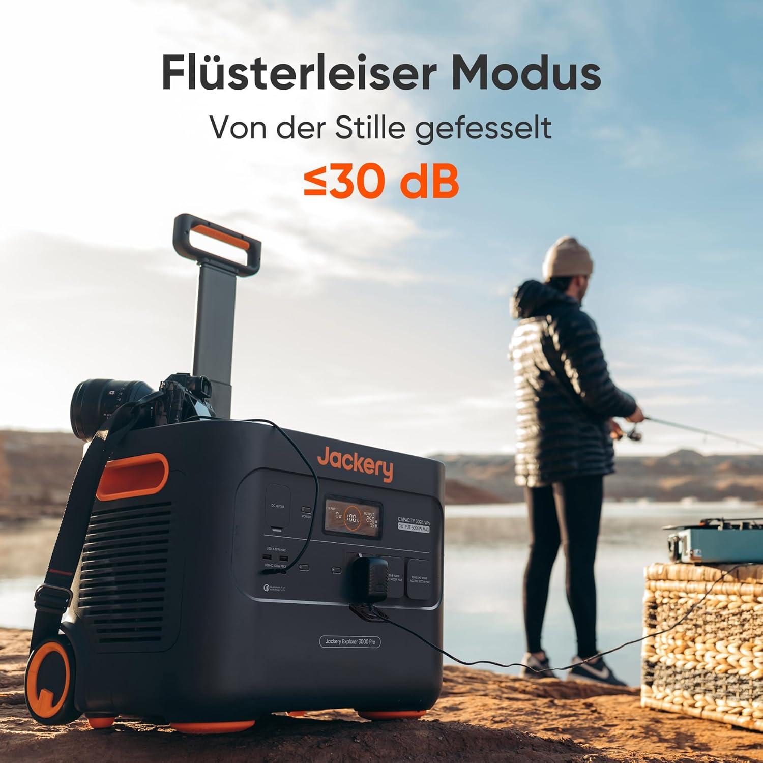 Ein Mann fischt an einem See mit einer Jackery-Powerstation. Die Station ist schwarz und orange, mit einer Kamera oben. Text: ≤30 dB.