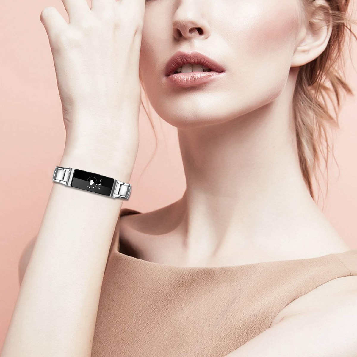 Eine Frau trägt einen Fitness-Tracker am Handgelenk. Der Tracker ist schwarz und silber und zeigt die Herzfrequenz an. Sie trägt ein hellbraunes Oberteil.