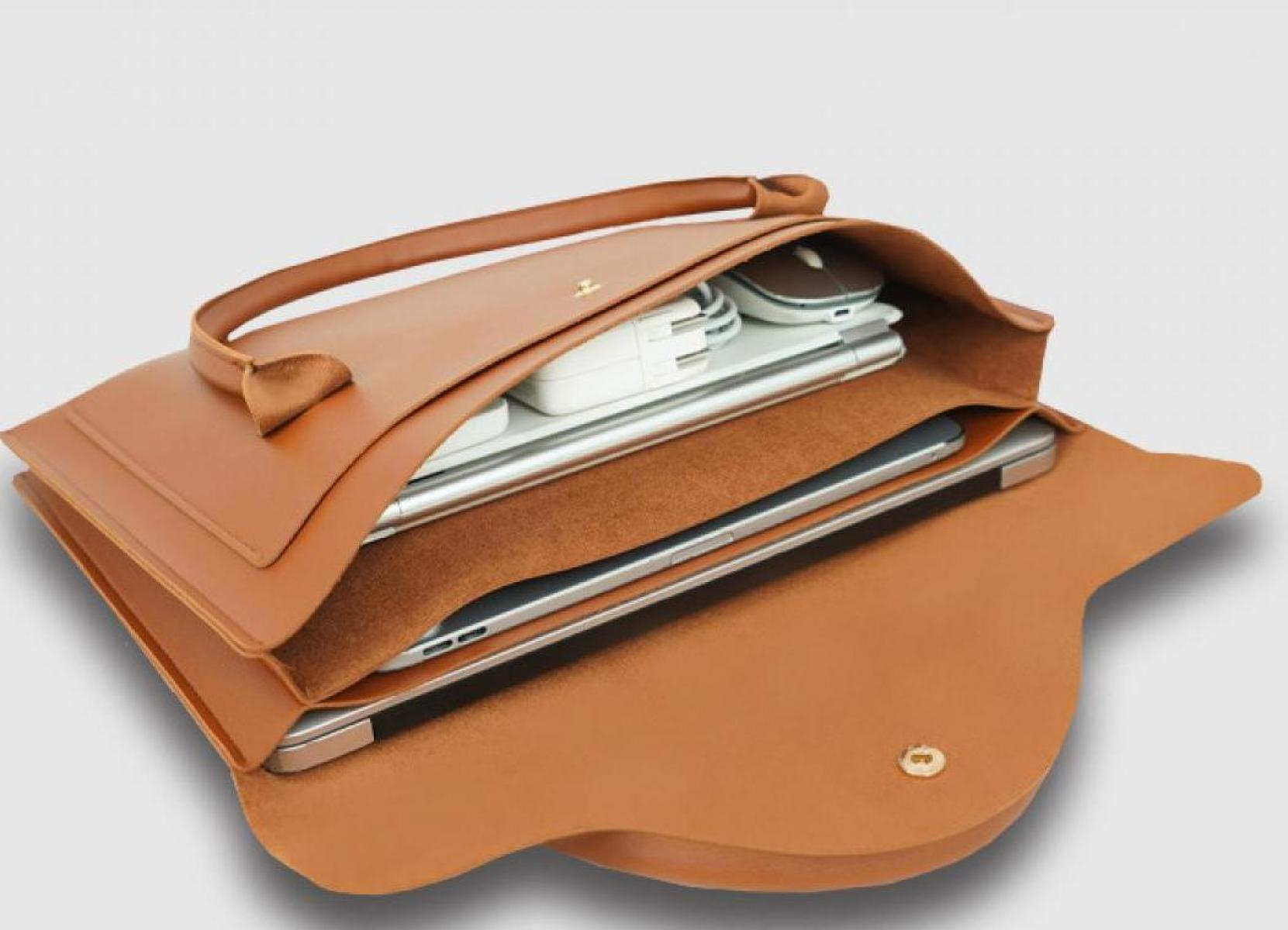 Geöffnete braune Ledertasche mit Griff, zeigt Elektronik wie Laptop, Maus und Ladegerät auf hellem Hintergrund.