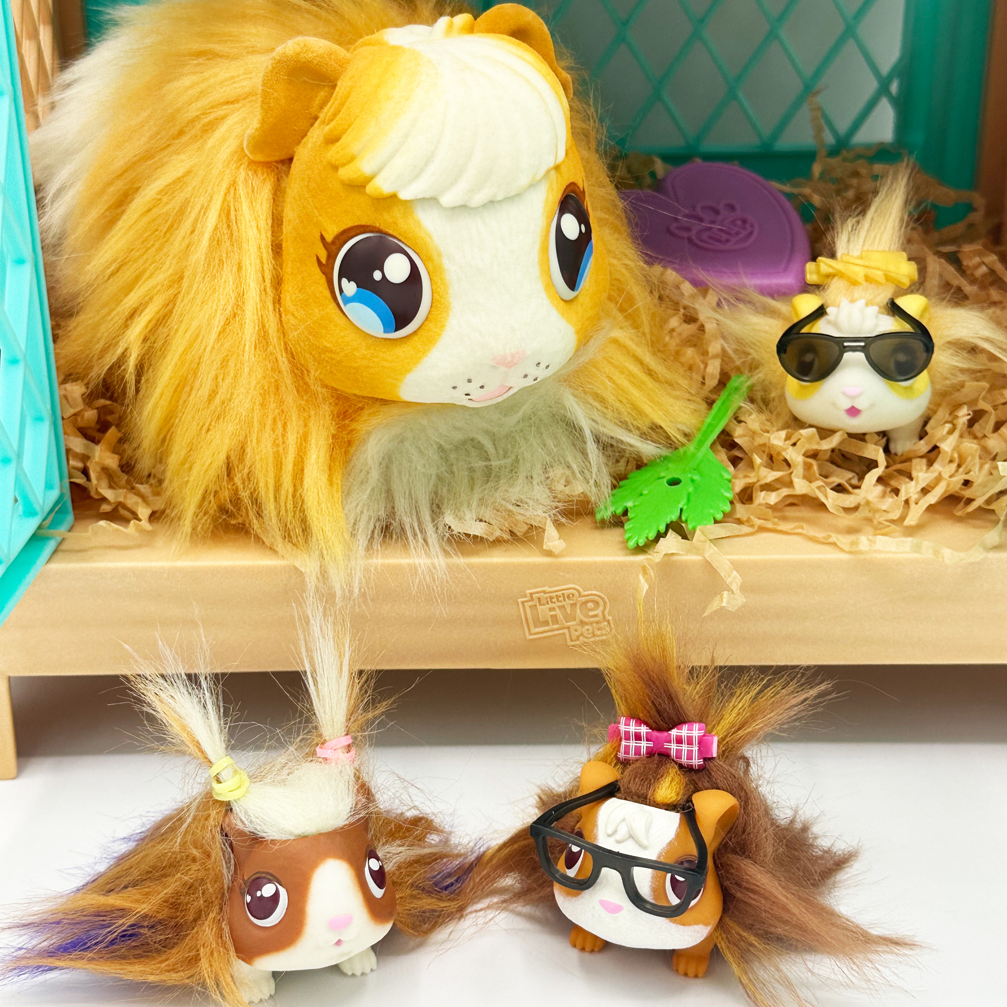 Zabawkowe świnki morskie w otoczeniu klatki. Niektóre noszą okulary przeciwsłoneczne i kokardy. Jedna duża świnka morska jest nad nimi.