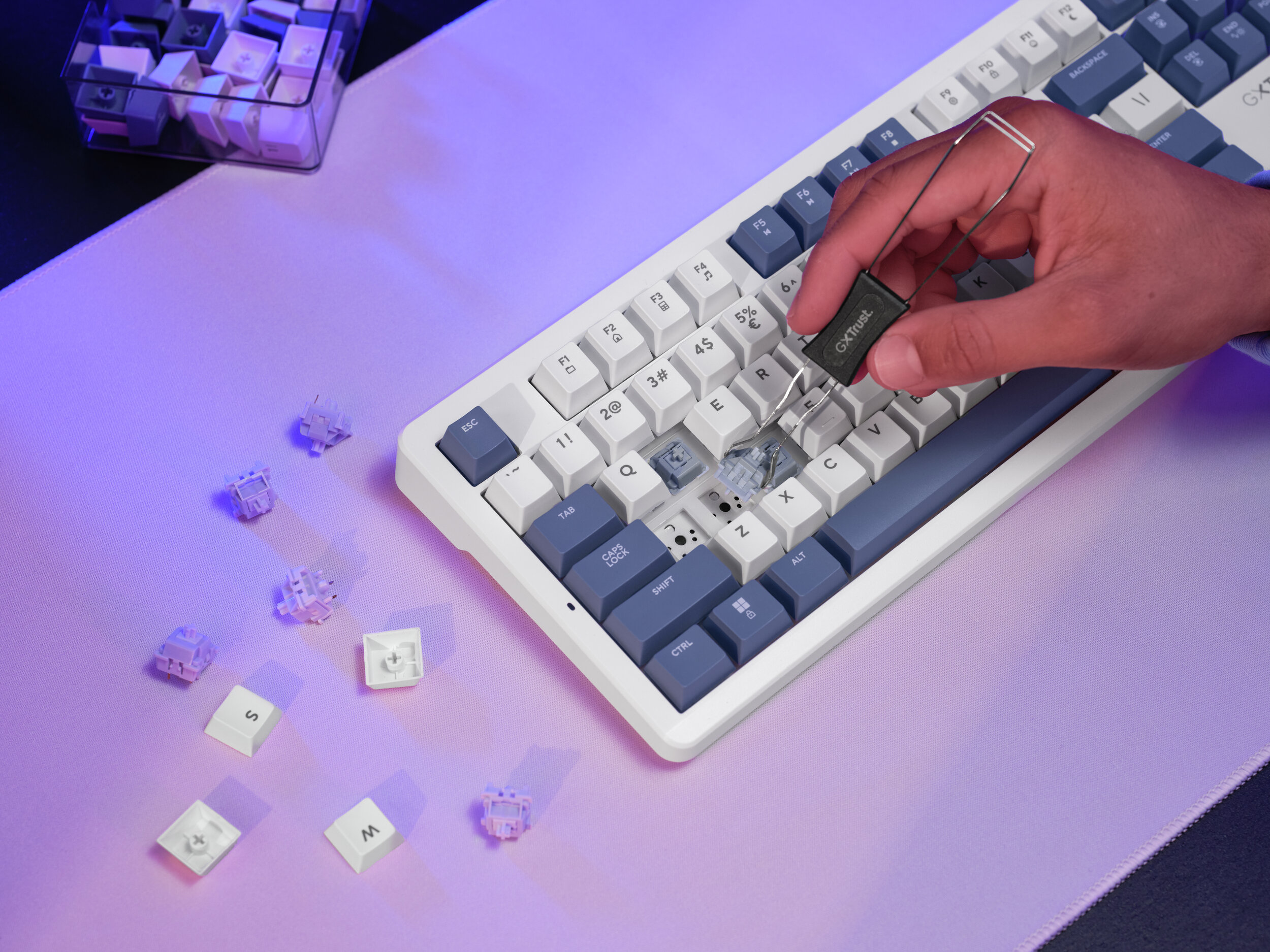 Hand entfernt eine Taste von einer Tastatur. Teile und Tasten liegen auf einer rosa Oberfläche verstreut.
