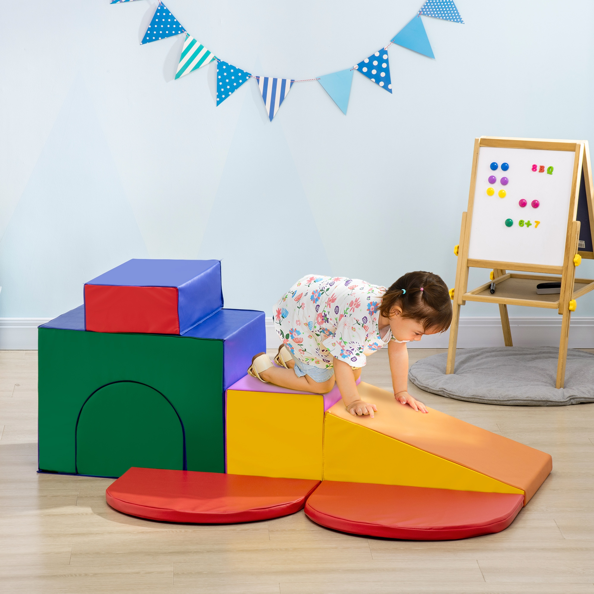 Un bambino piccolo si arrampica su blocchi gioco colorati. Dietro, una lavagna con magneti e uno striscione.