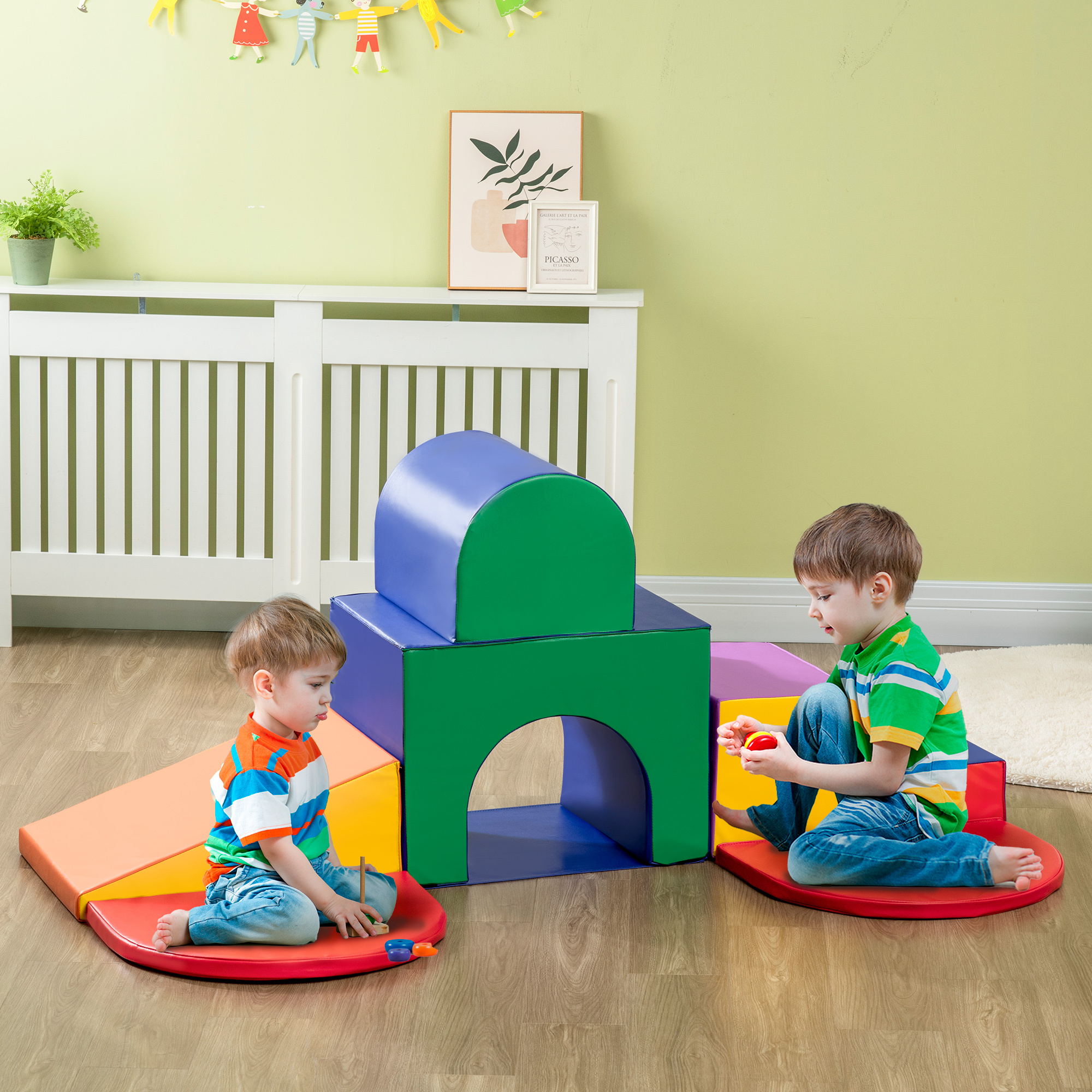 Due bambini giocano con blocchi di schiuma colorati. Un bambino tiene un giocattolo. Lo sfondo ha un radiatore bianco e arte murale.