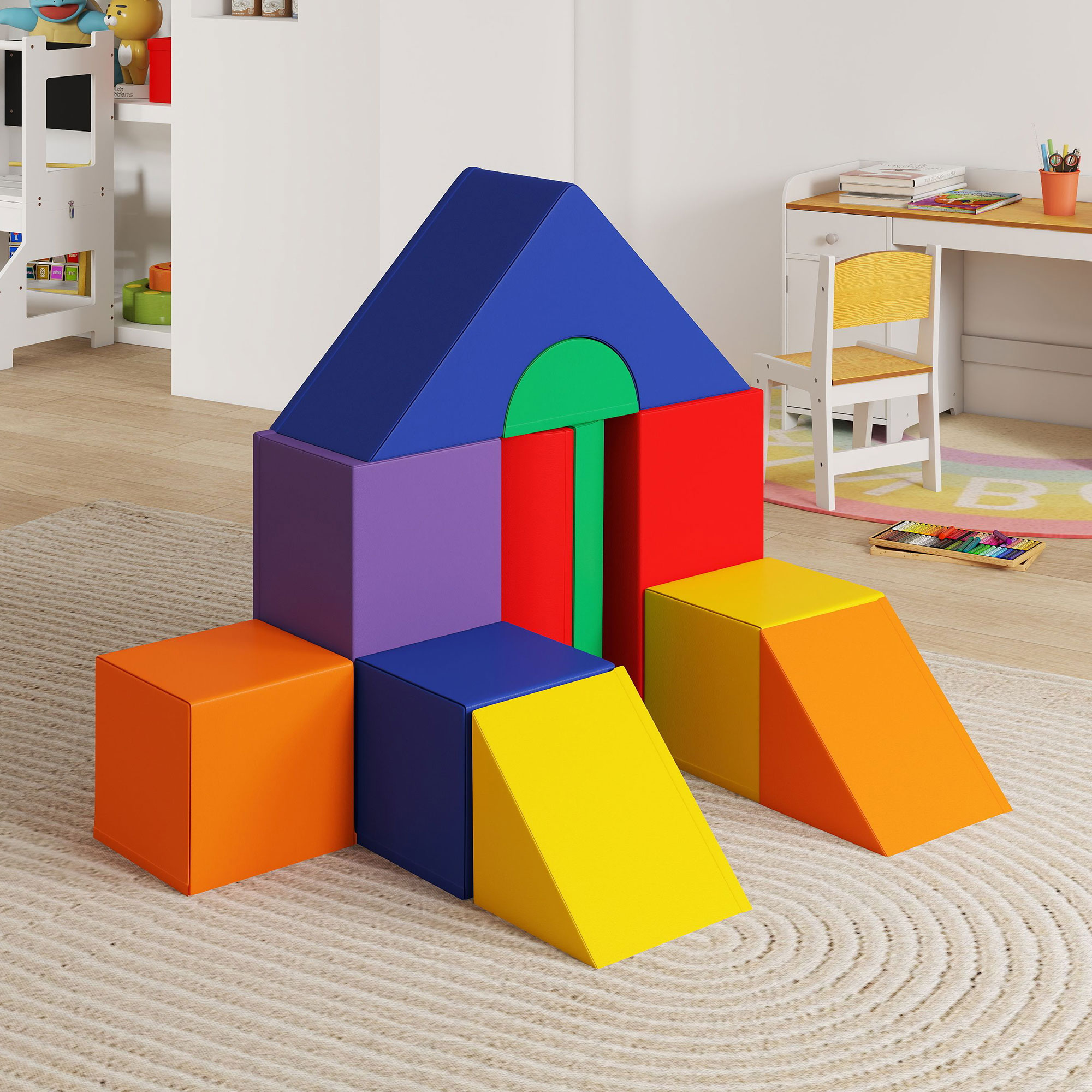 Blocchi di schiuma colorati disposti come una casa e rampe su un tappeto beige, con scrivania e sedia sullo sfondo.