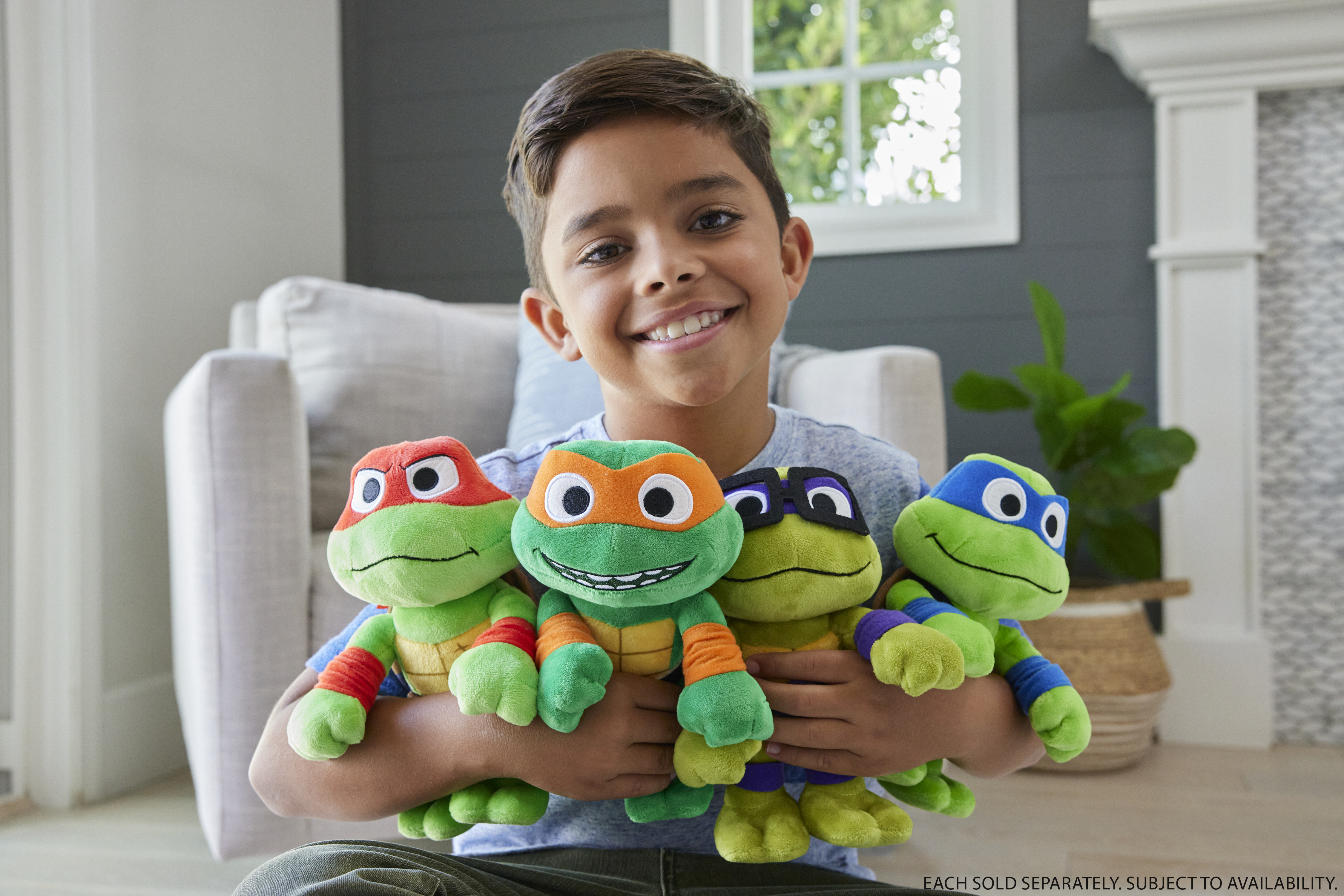 Ein lächelnder Junge hält vier Teenage Mutant Ninja Turtle-Plüschtiere. Die Schildkröten haben verschiedenfarbige Masken.