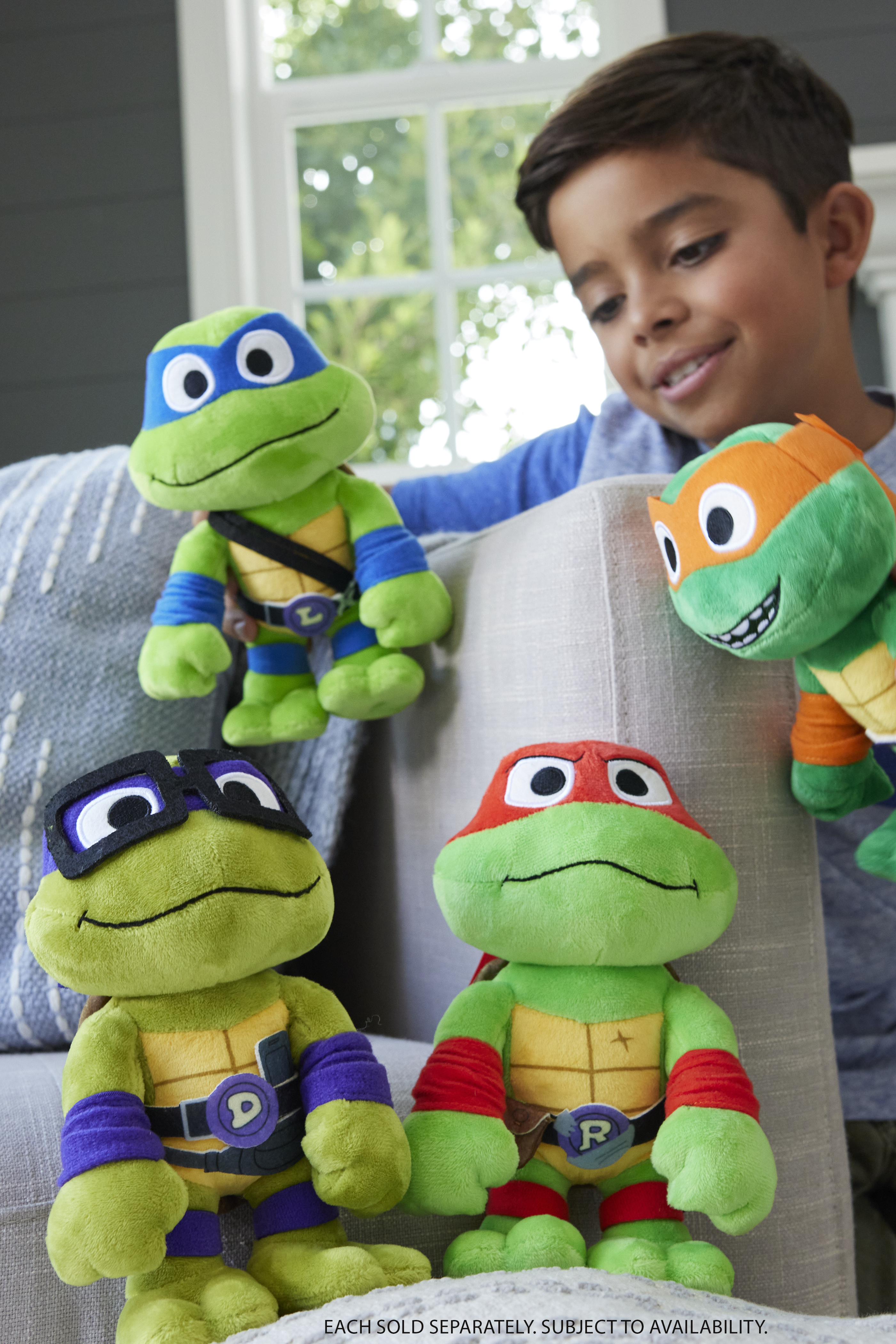 Ein Junge hält vier Teenage Mutant Ninja Turtles-Plüschtiere. Jeder hat eine andersfarbige Maske.