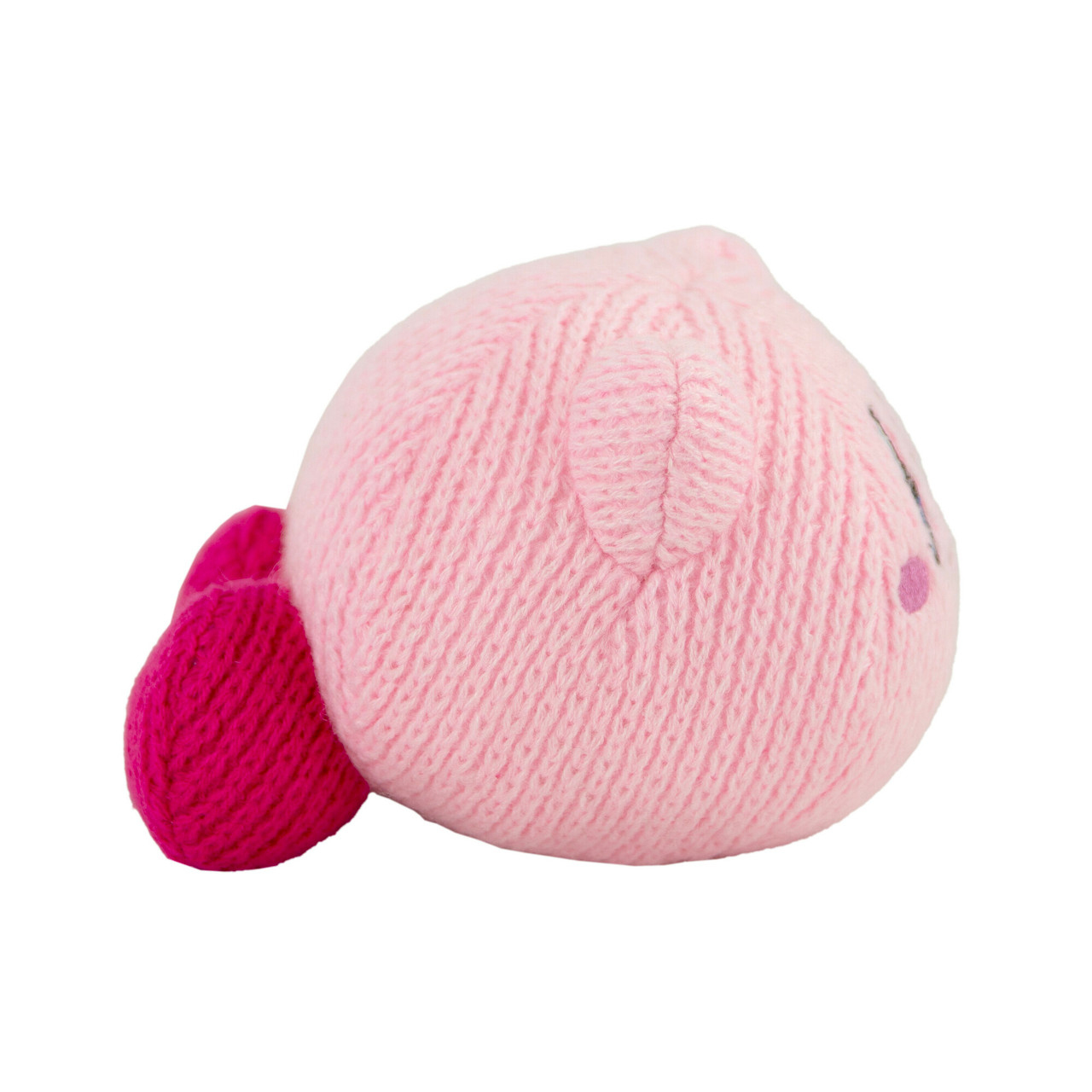 Un peluche di Kirby lavorato a maglia è mostrato, principalmente rosa con un piede rosa più scuro. Ha piccoli occhi e un punto per una guancia.
