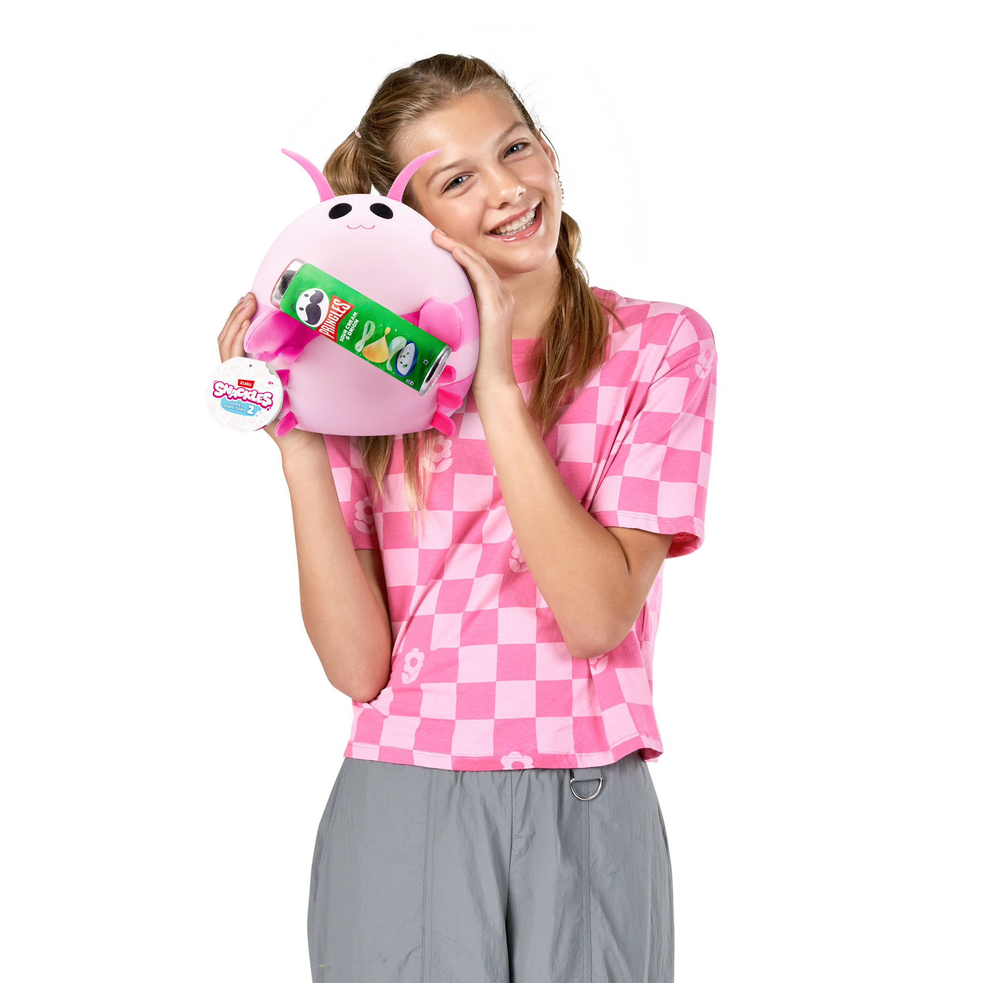 Ein lächelndes Mädchen hält ein rosa Plüschtier mit einer Pringles-Dose. Sie trägt ein rosa kariertes Hemd und graue Hose.