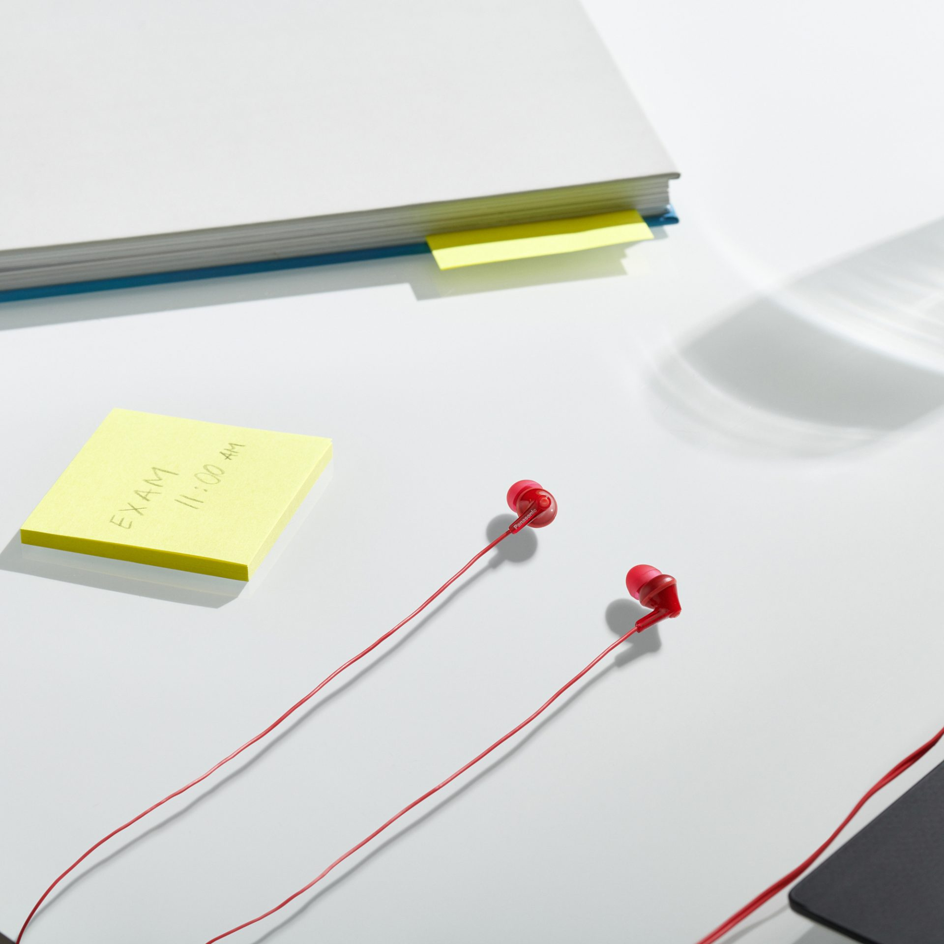 Czerwone słuchawki, żółte karteczki samoprzylepne z napisem 'EXAM 11:00 AM' i książka z żółtą zakładką.