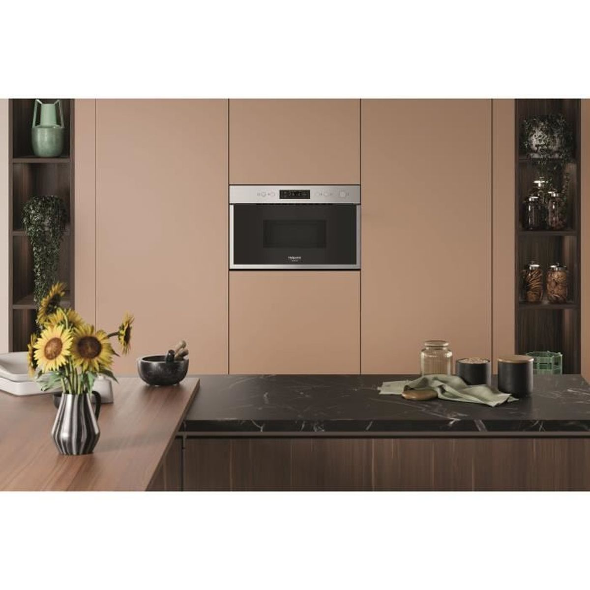 Cucina con forno a microonde. Girasoli in un vaso. Armadi e piano di lavoro. Barattoli sugli scaffali.