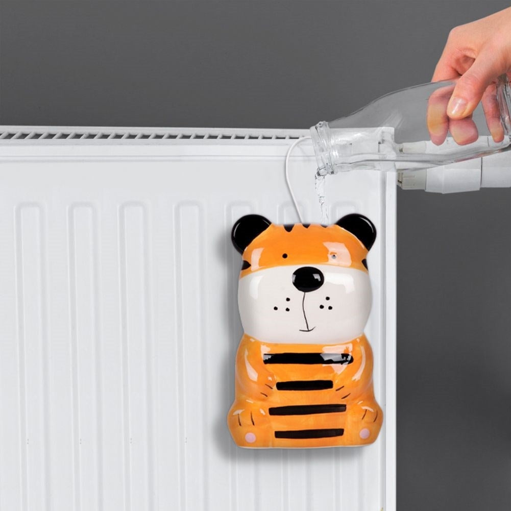 Un humidificador con forma de tigre se llena de agua de una botella de vidrio. Cuelga de un radiador blanco.