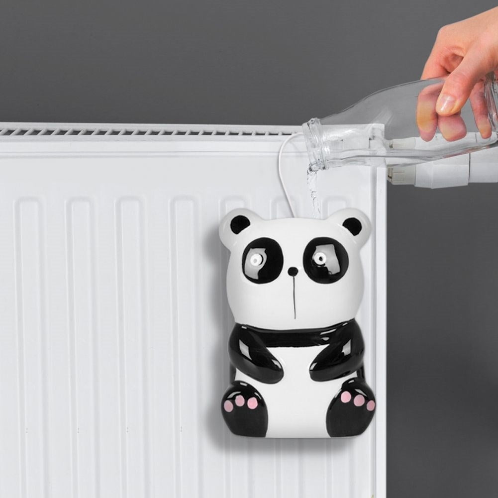 Un humidificador con forma de panda se llena de agua de una botella. Cuelga de un radiador blanco contra una pared gris.