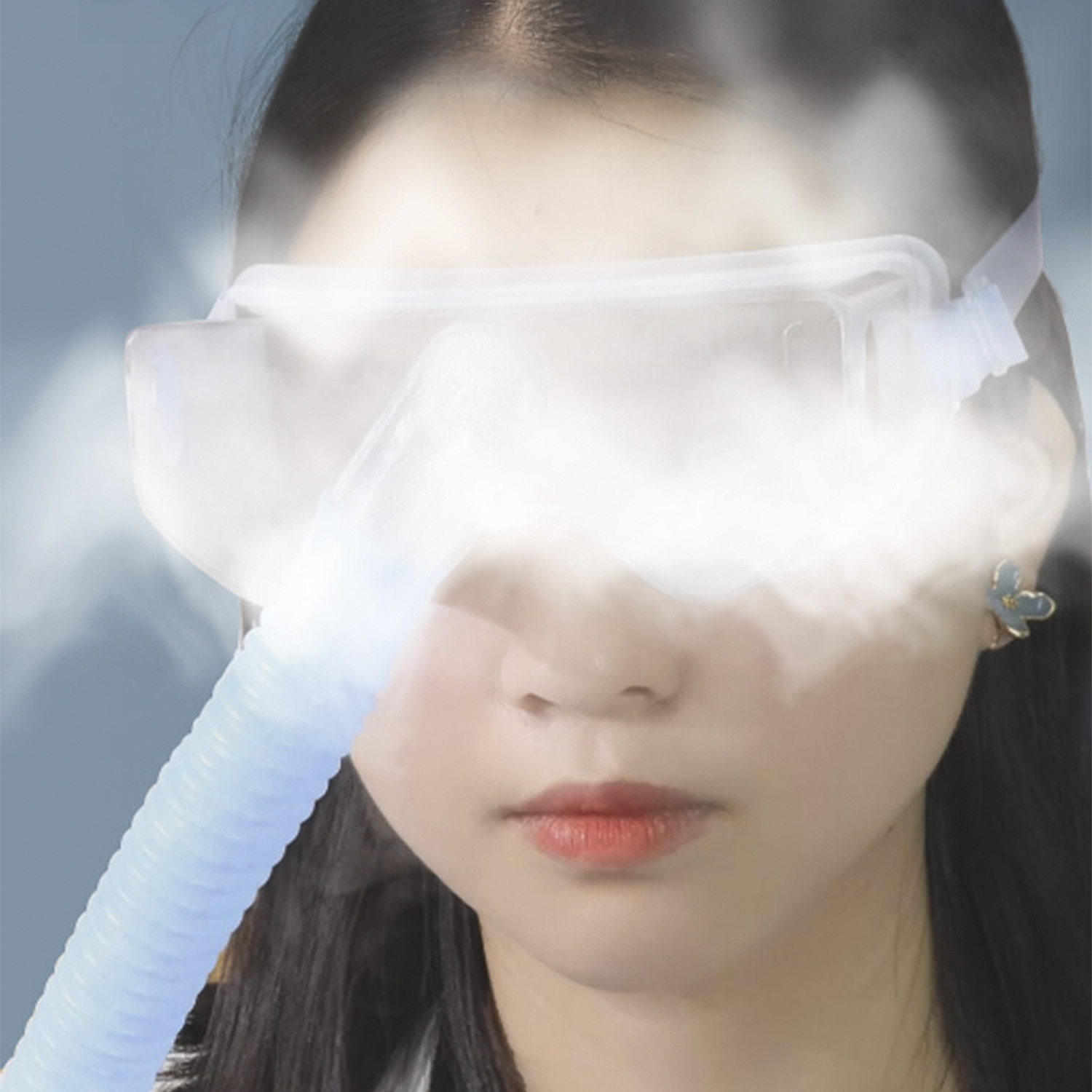 Una donna con una maschera facciale e un tubo blu. Vapore bianco oscura il viso. Ha i capelli scuri e un orecchino a fiore.