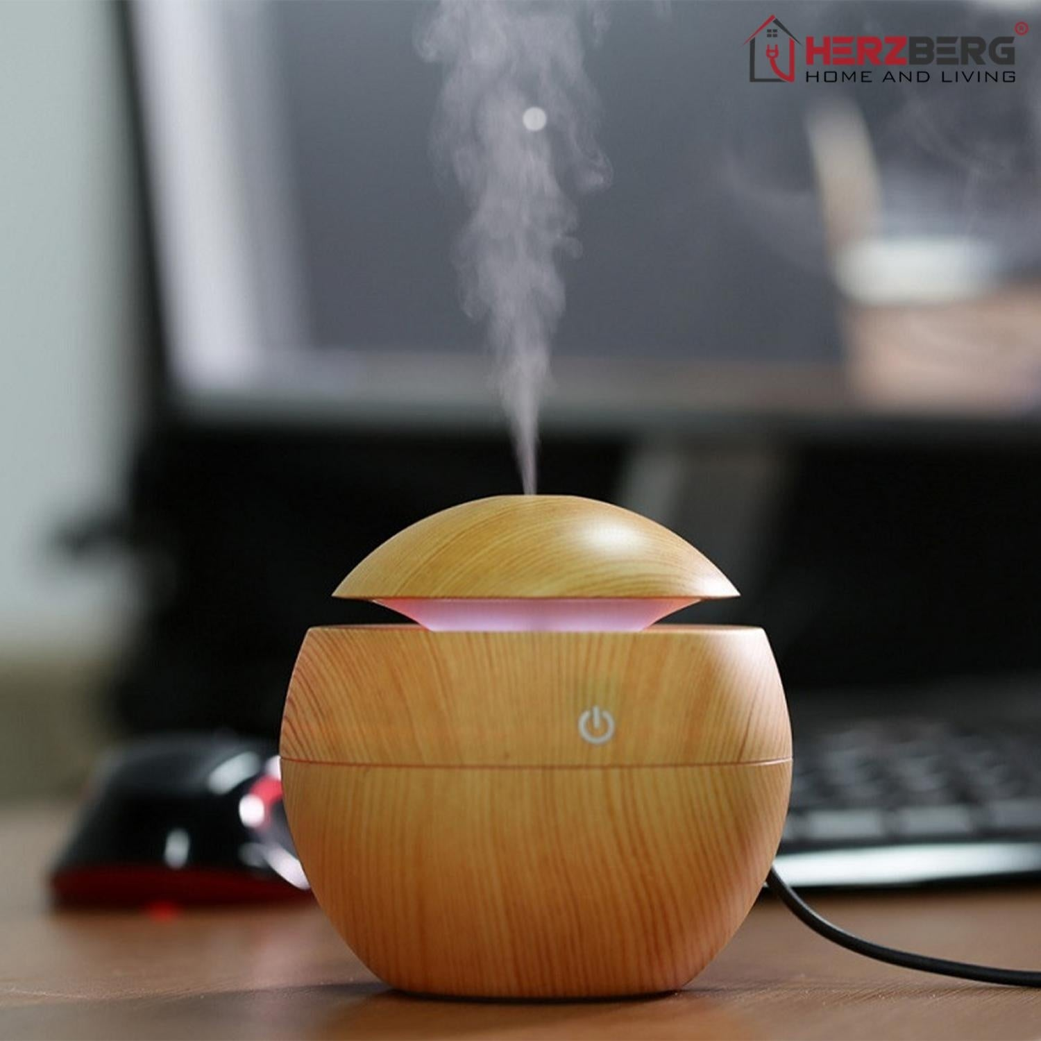 Un difusor de aceites esenciales de madera con vapor ascendente. Un logotipo está en la parte superior derecha. Un portátil y un ratón están al fondo.