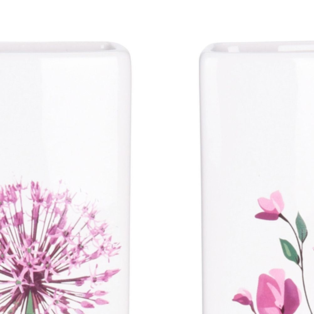Dos jarrones blancos con diseños florales. Uno tiene un allium morado, el otro flores rosas y hojas verdes.