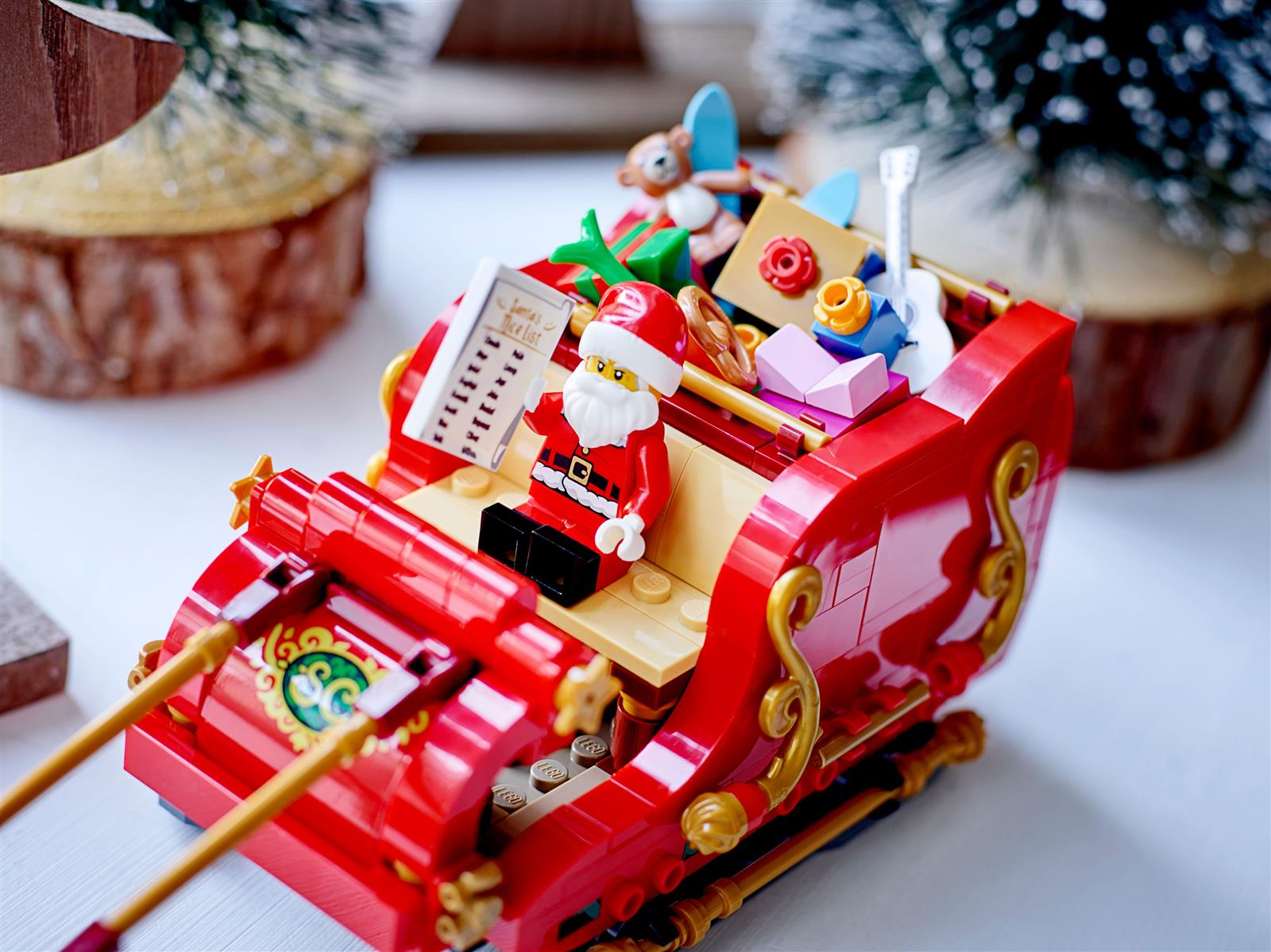 Ein Lego-Weihnachtsmann in einem roten Schlitten mit Geschenken. Eine To-Do-Liste liegt neben ihm. Weihnachtsbäume sind im Hintergrund.