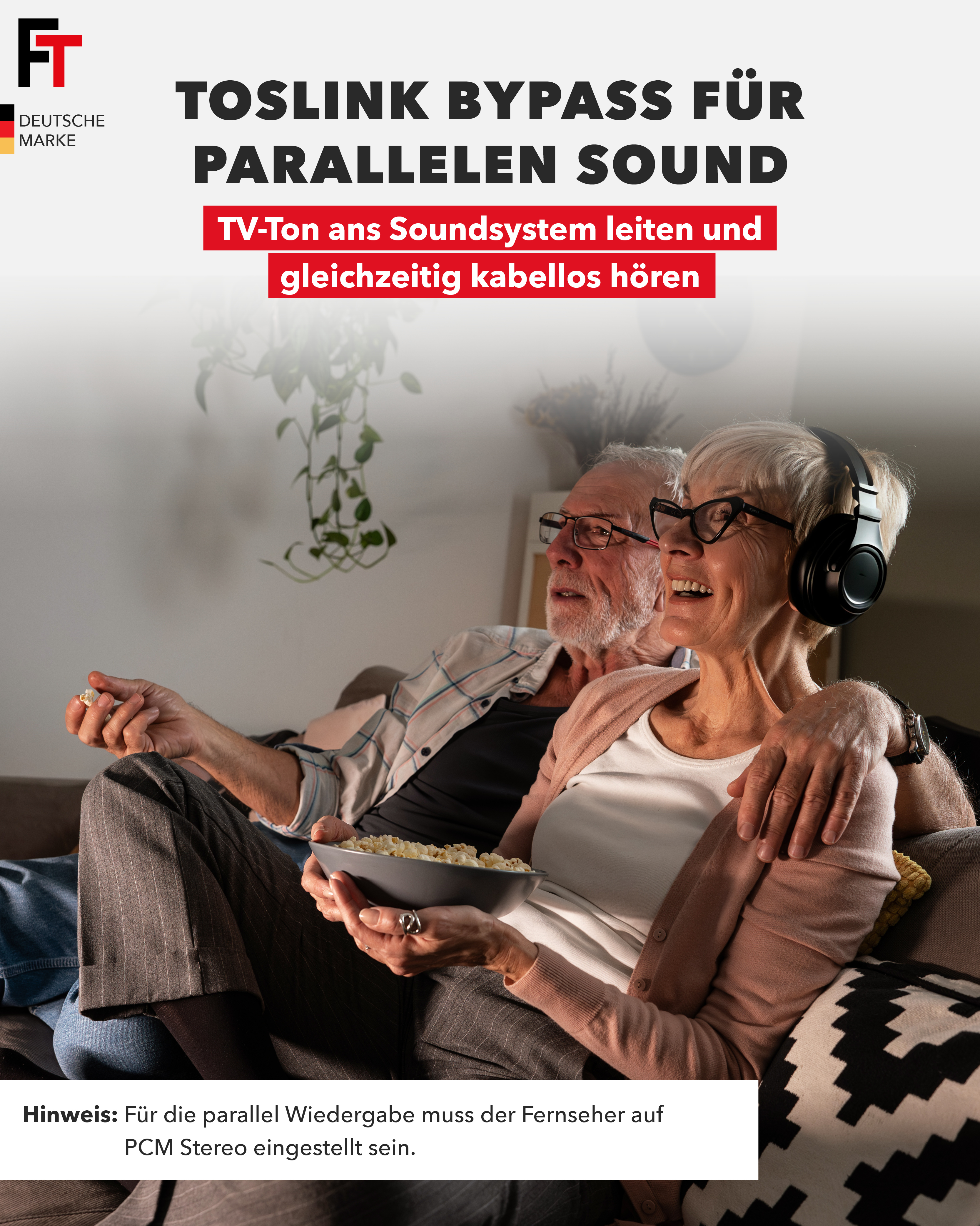 Ein älteres Ehepaar schaut auf einer Couch fern. Die Frau trägt Kopfhörer und hält eine Schüssel Popcorn.