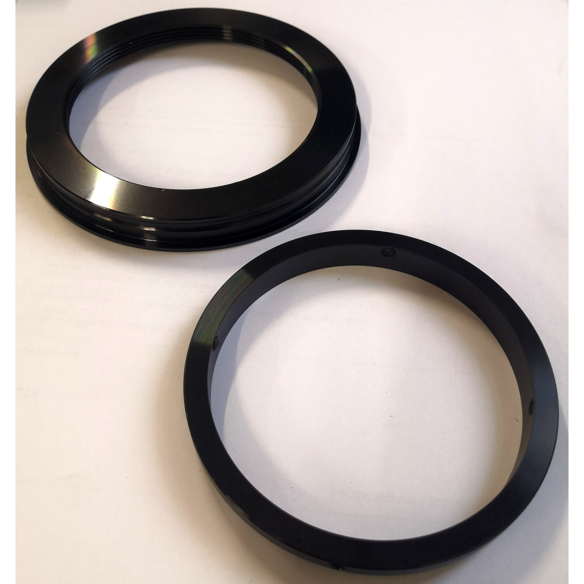 Zwei schwarze, kreisförmige Metallringe auf weißem Untergrund. Ein Ring hat Rillen.