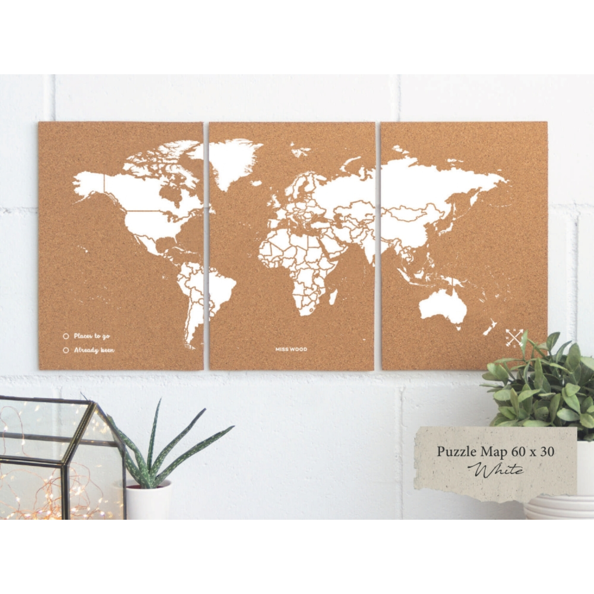 Eine Weltkarte aus Kork mit weißen Kontinenten an einer weißen Wand. Ein Schild zeigt 'Puzzle Map 60 x 30 White'.