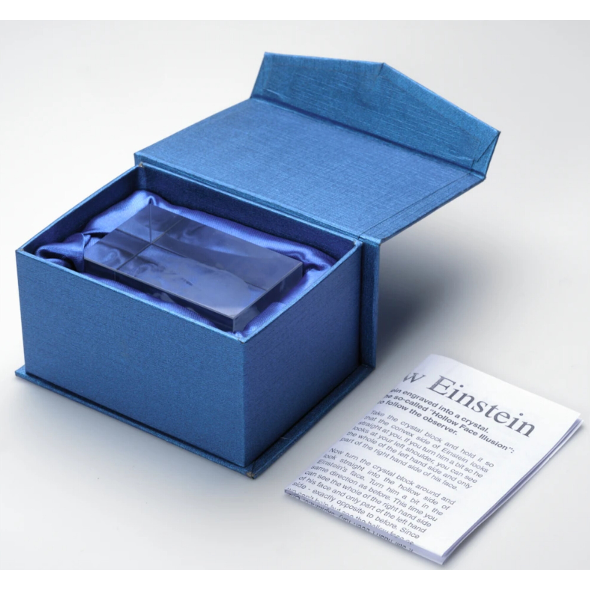 Blaue Box mit offenem Deckel, die einen Kristall enthält. Ein Papier mit Text liegt daneben.