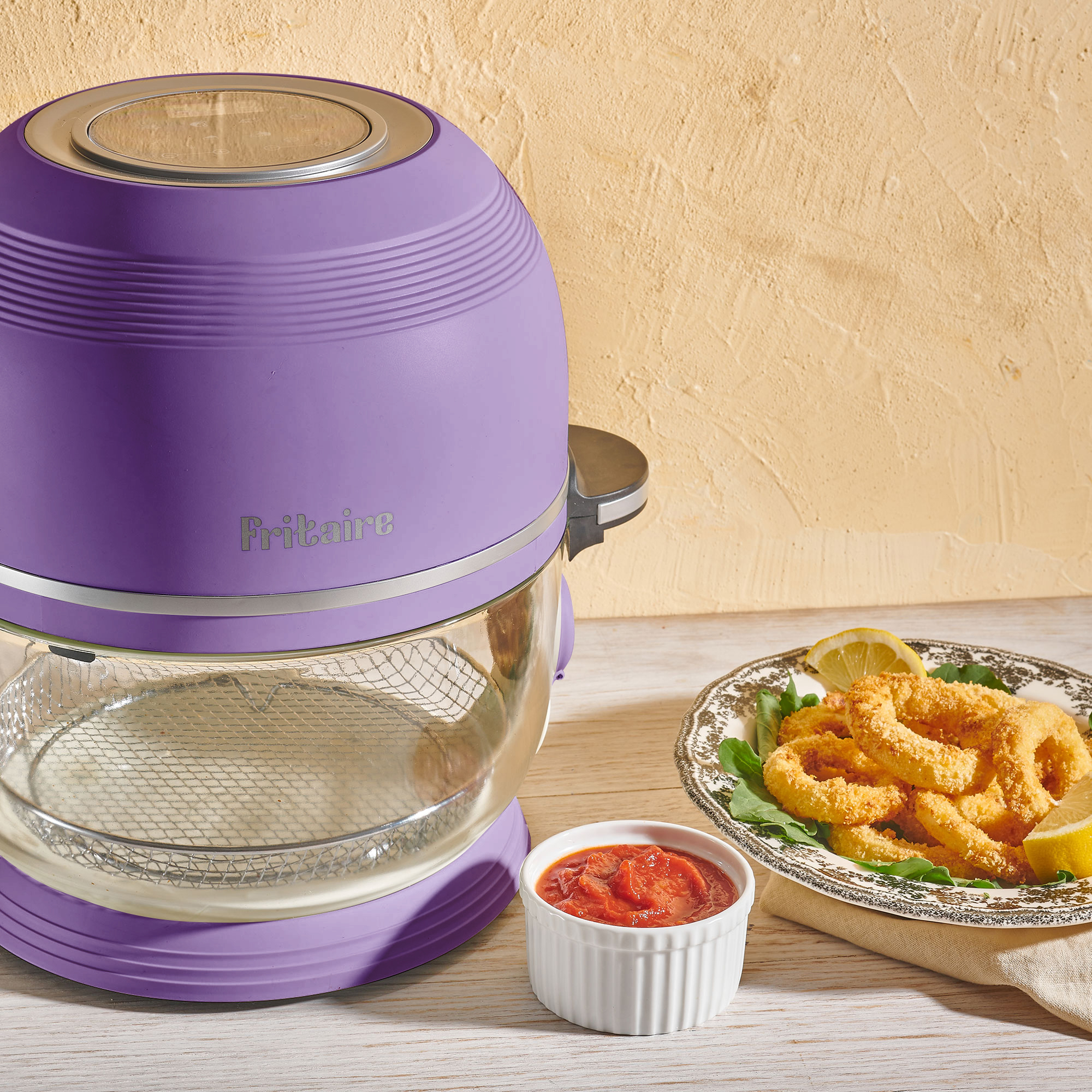 Ein lila Airfryer mit frittierten Calamari, Zitronenspalten und Tomatensauce auf einem Holztisch.