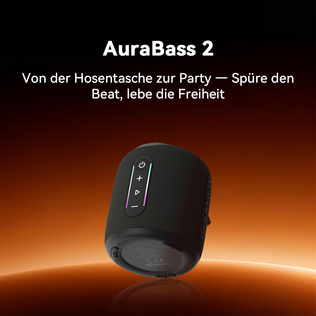 Ein schwarzer AuraBass 2 Lautsprecher mit Steuertasten steht auf einer reflektierenden Oberfläche. Der Hintergrund ist ein orangefarbener Farbverlauf.