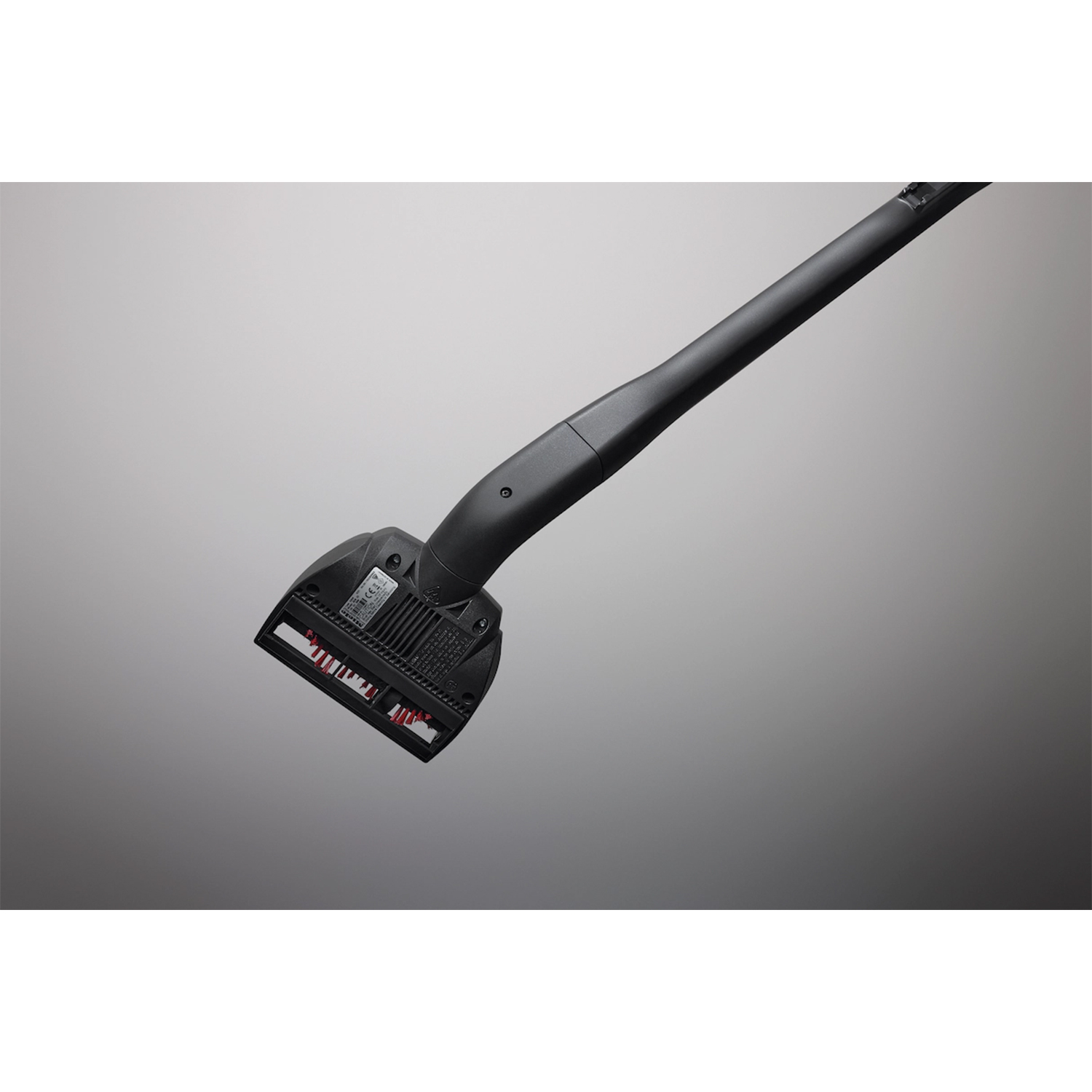 Czarna głowica i uchwyt odkurzacza na szarym tle gradientowym. Czerwone włosie jest widoczne na głowicy.