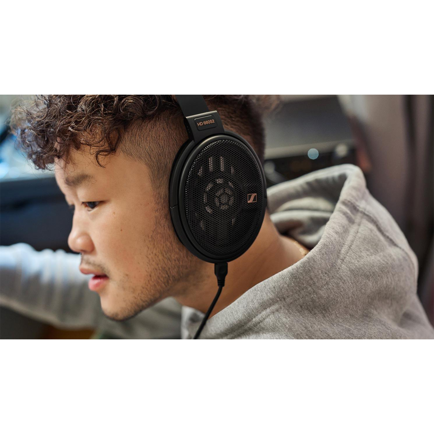 Ein Mann mit schwarzen Kopfhörern. Er hat kurze, lockige Haare und einen grauen Kapuzenpullover. Die Kopfhörer sind Sennheiser HD 660S2.