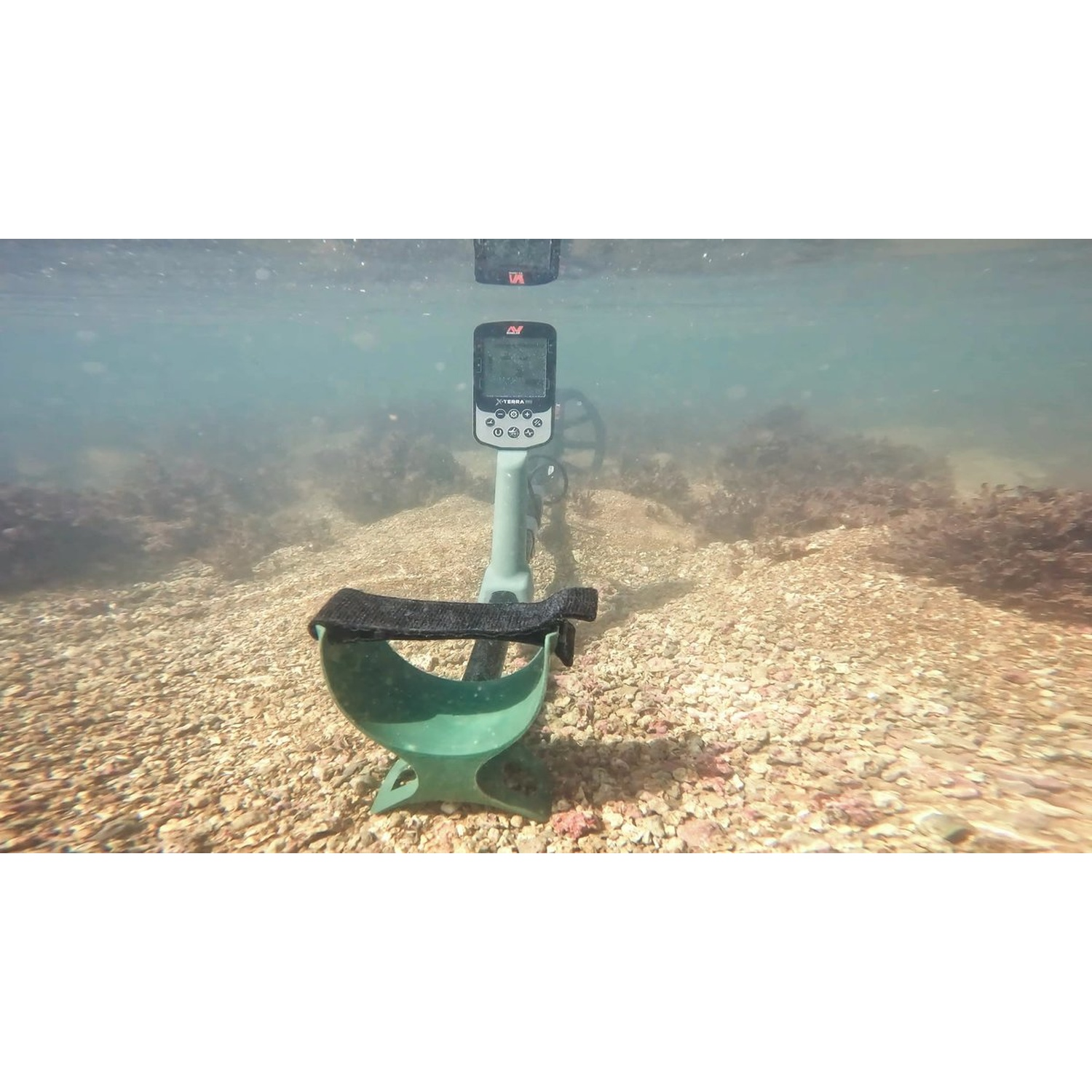 Ein Unterwasser-Metalldetektor im Meer. Das Gerät ist grün und schwarz. Der Meeresboden ist sandig und steinig.