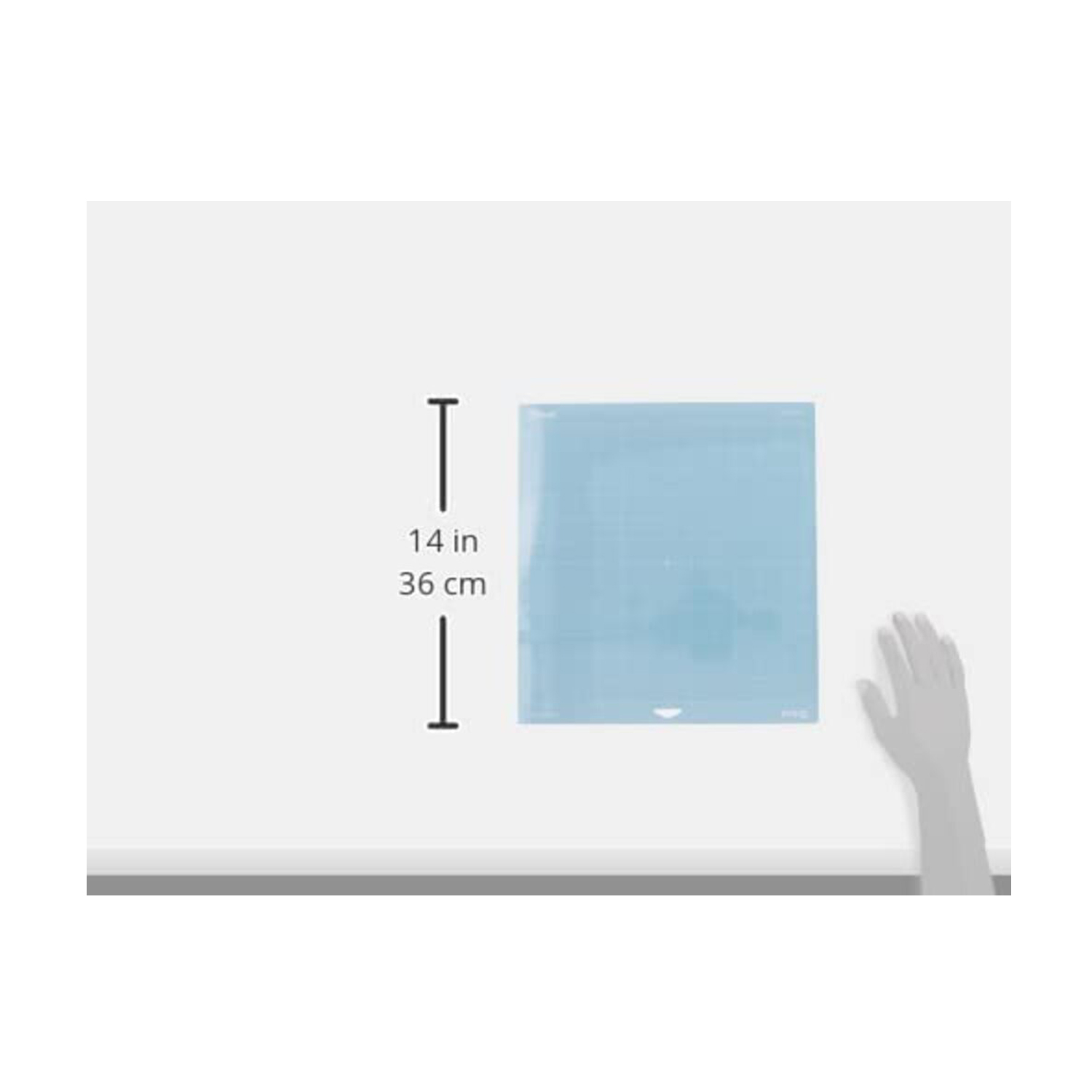 Eine hellblaue Schneidematte liegt auf einer weißen Oberfläche. Eine Hand greift danach. Die Matte hat Maße in Zoll und Zentimetern.
