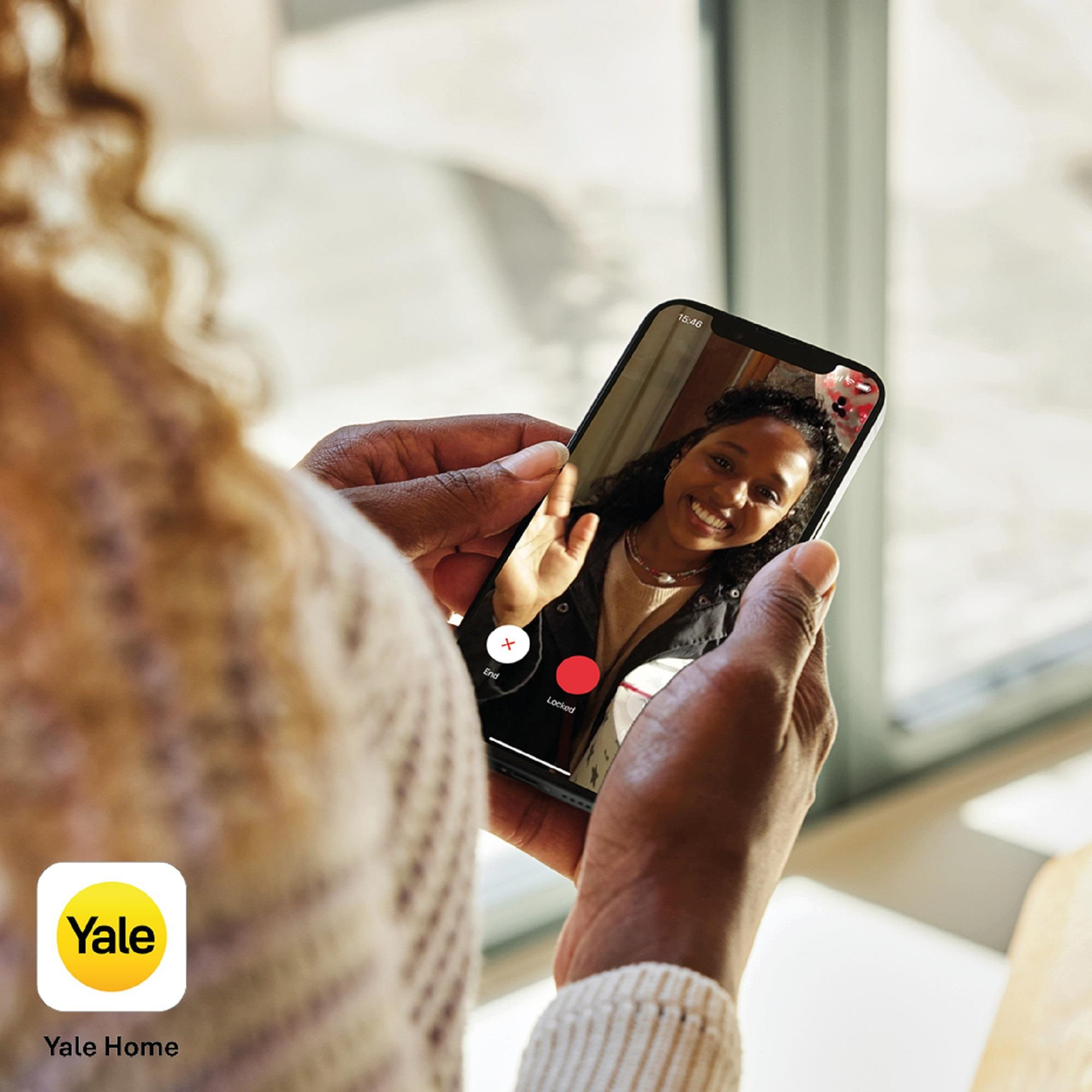 Persona sosteniendo teléfono con videollamada. Mujer en pantalla saluda. Logo Yale Home abajo a la izquierda.